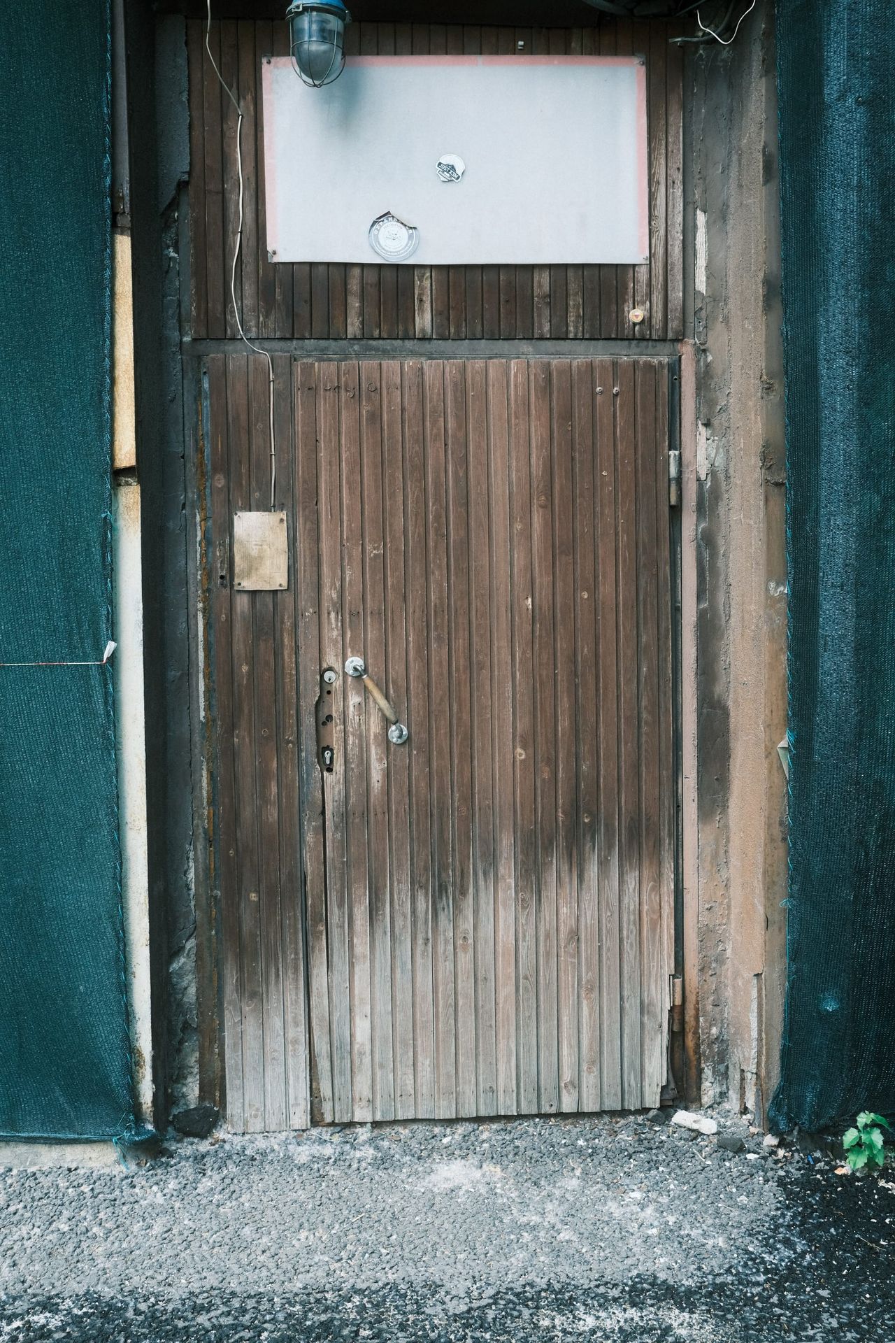 A weathered wooden door with a blank pale panel and a hanging light above it in a dark Moscow doorway.