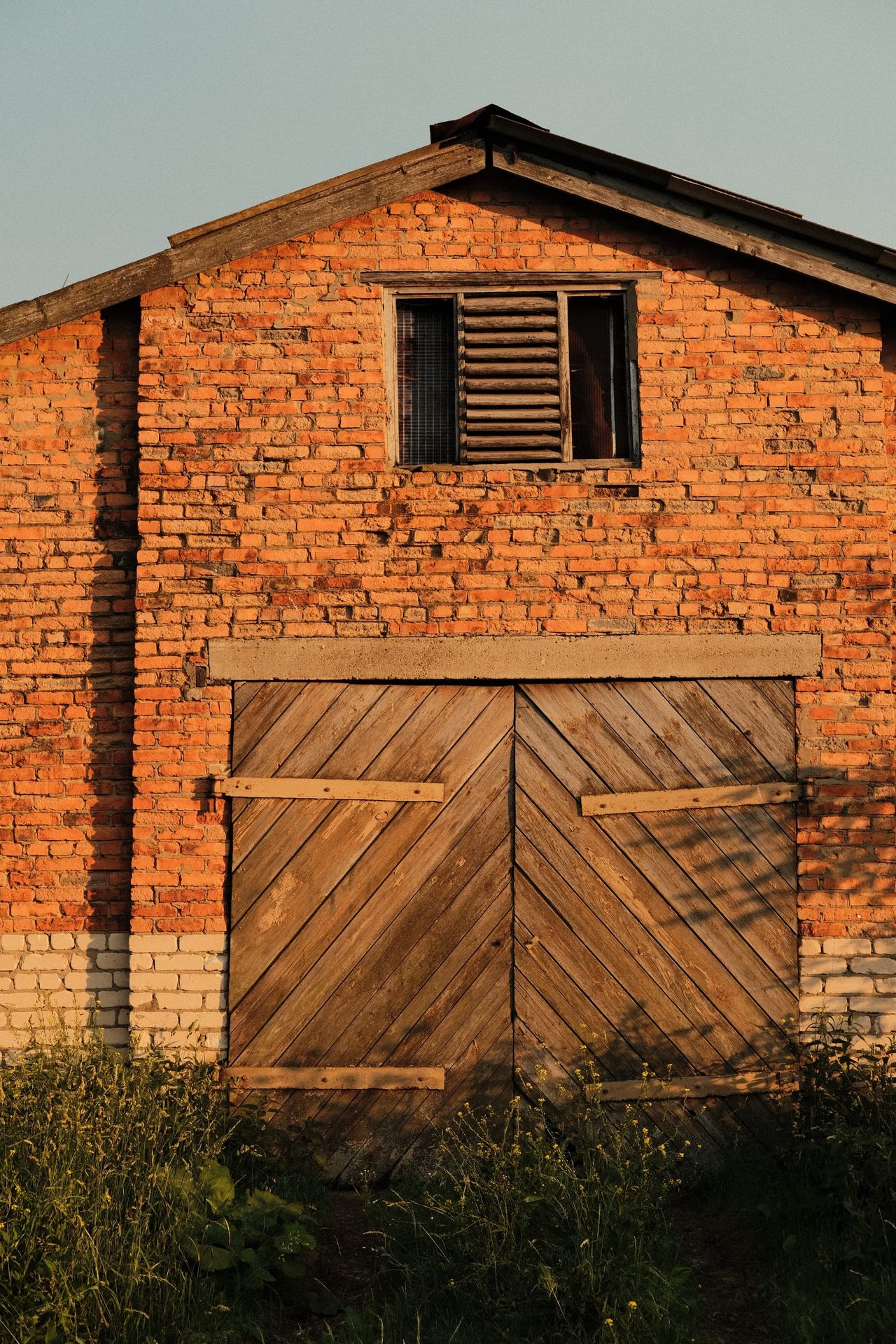 A red-brick farm building with closed wooden doors and a small dark upper window.
