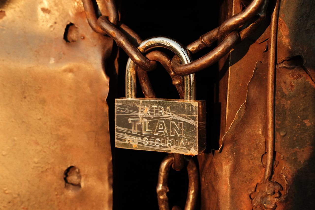 A brass-coloured padlock and heavy chain secure a rusty metal door in warm evening light.