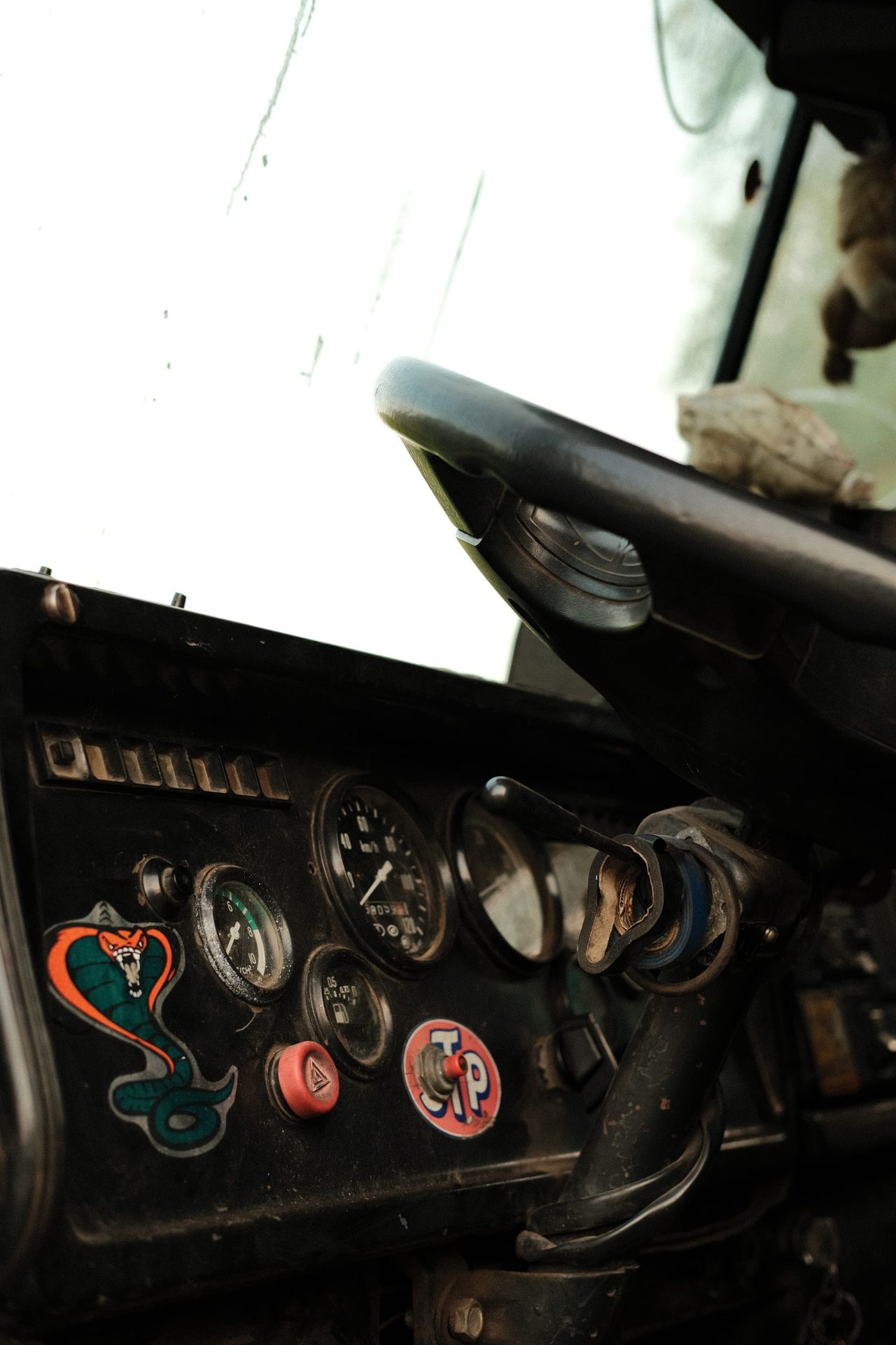 Close view of the steering wheel, gauges and colourful stickers inside an old truck cab.