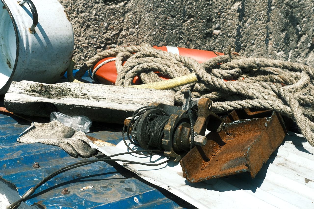 Coiled ropes, an orange life ring and worn deck equipment lie on a small boat’s blue-painted deck.