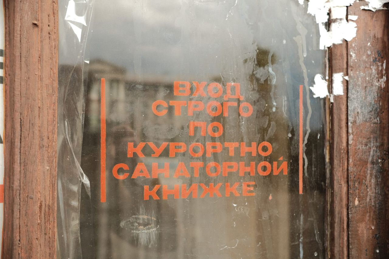 Faded orange Cyrillic lettering remains on a dark wooden-framed window of an old resort building.