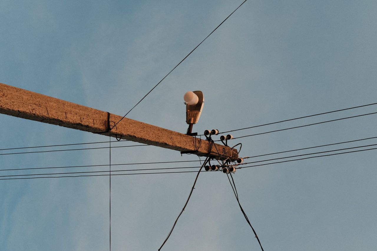 Weathered utility crossarm carries an insulator and clustered overhead wires.