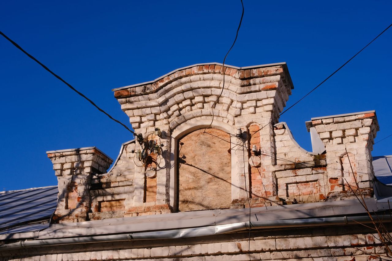 Weathered brick parapet and sealed arch crossed by overhead wires.