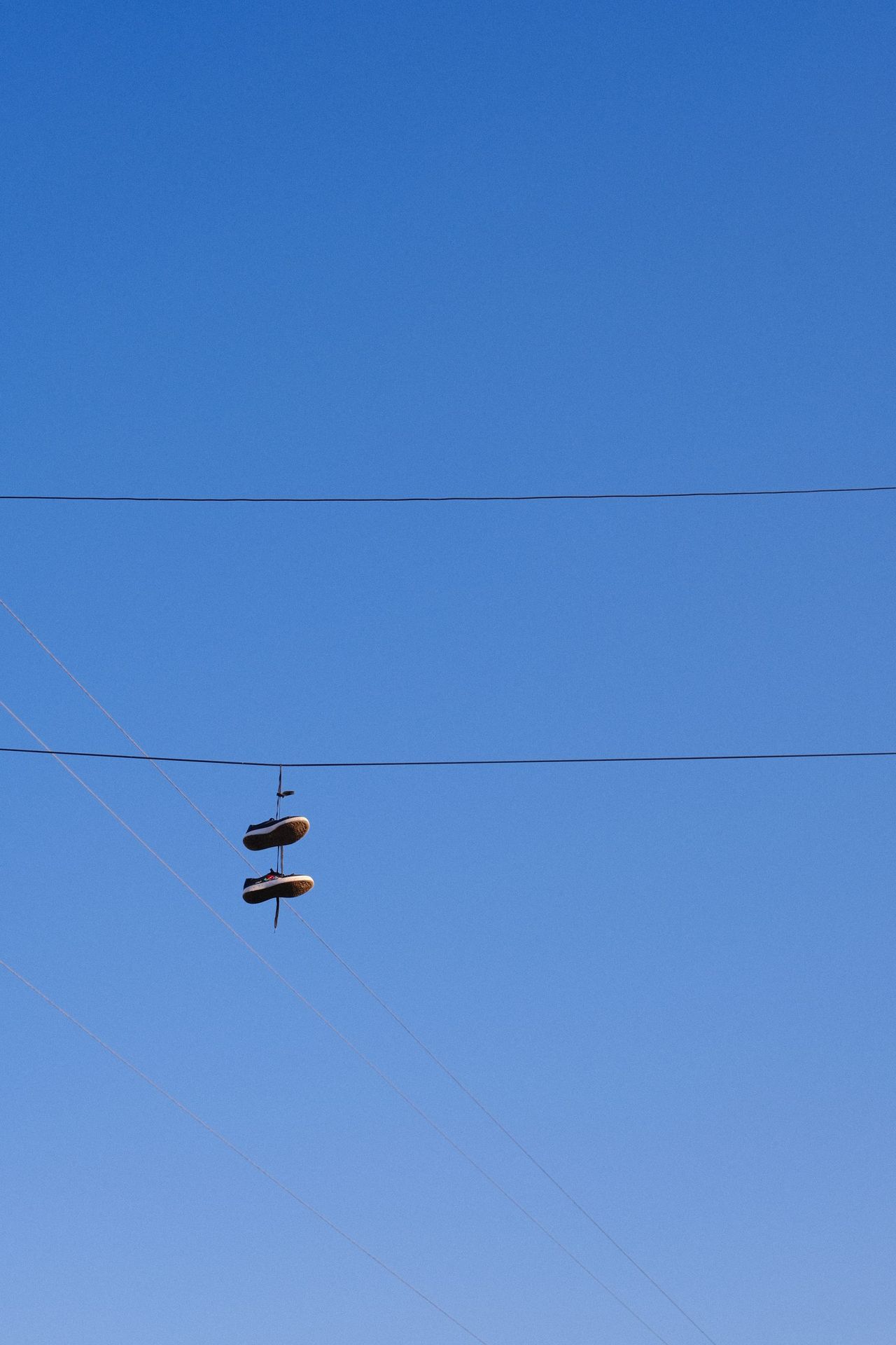 Unos zapatos atados cuelgan de un cable bajo un cielo azul despejado.