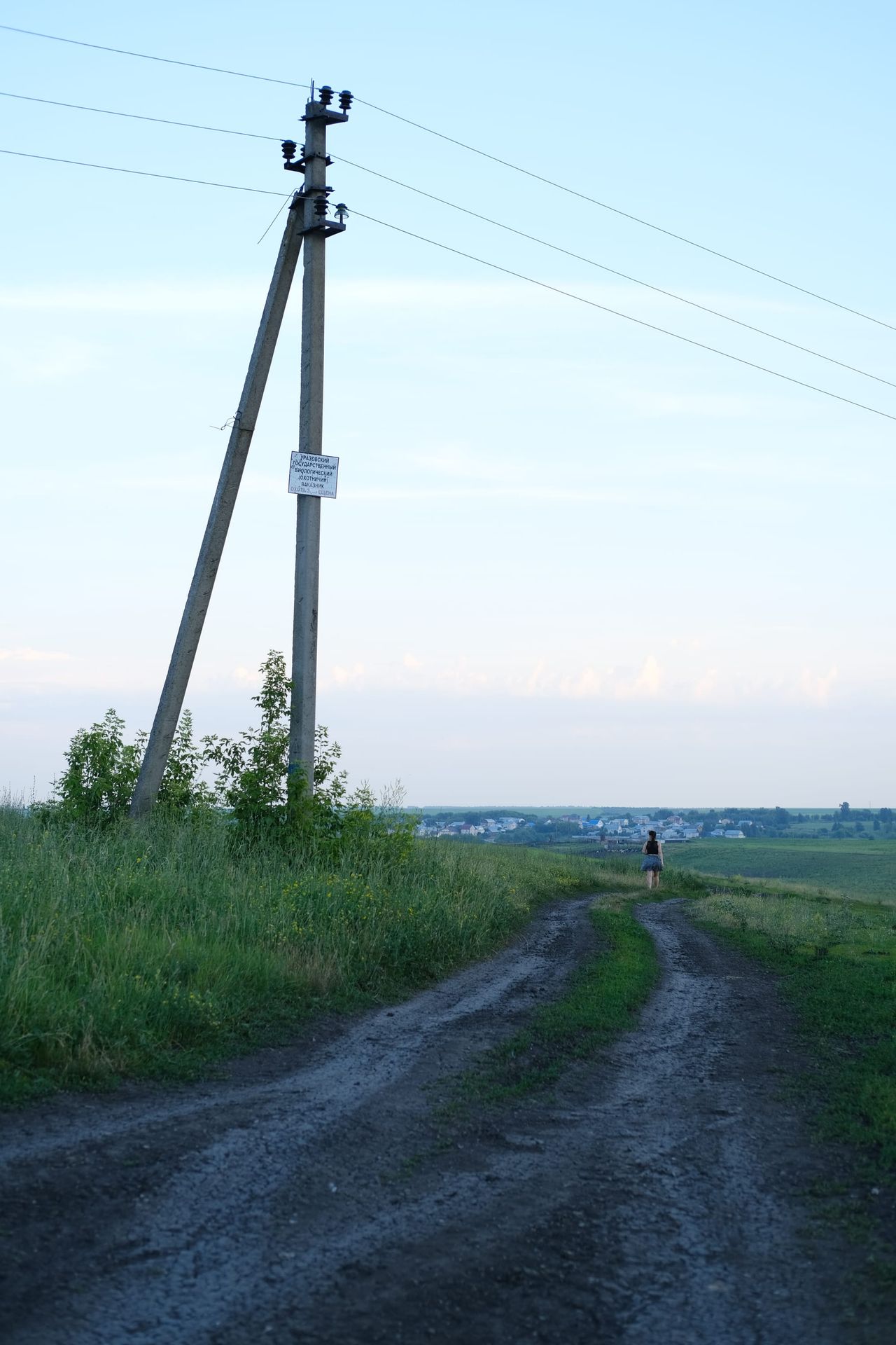 Rural dirt track follows utility poles toward a distant walker.