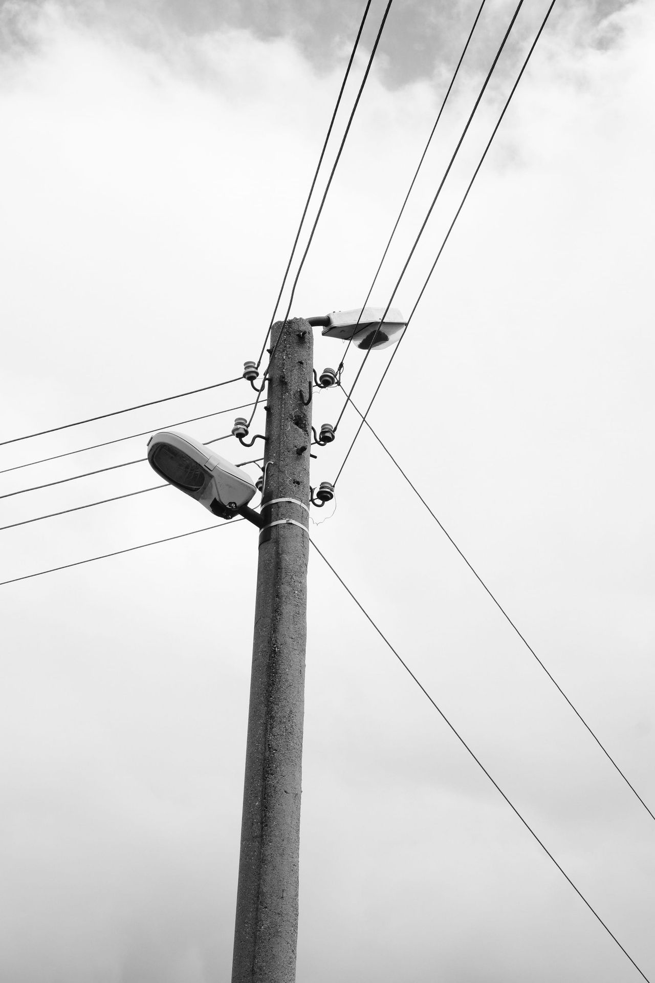 曇り空の下に曲がった街灯を備えたコンクリート電柱が立つ。
