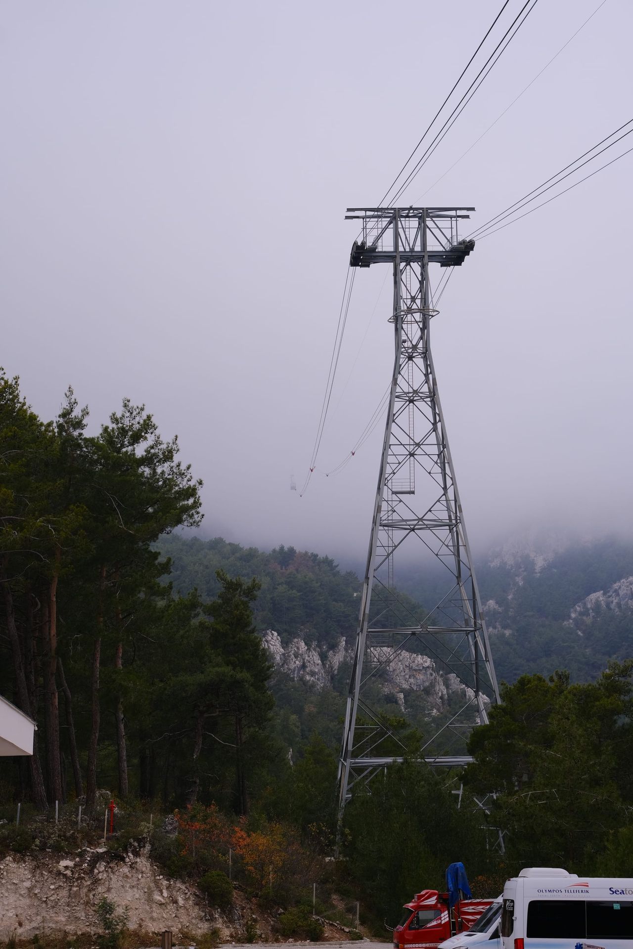 Electricity pylon rises above misty wooded hills.