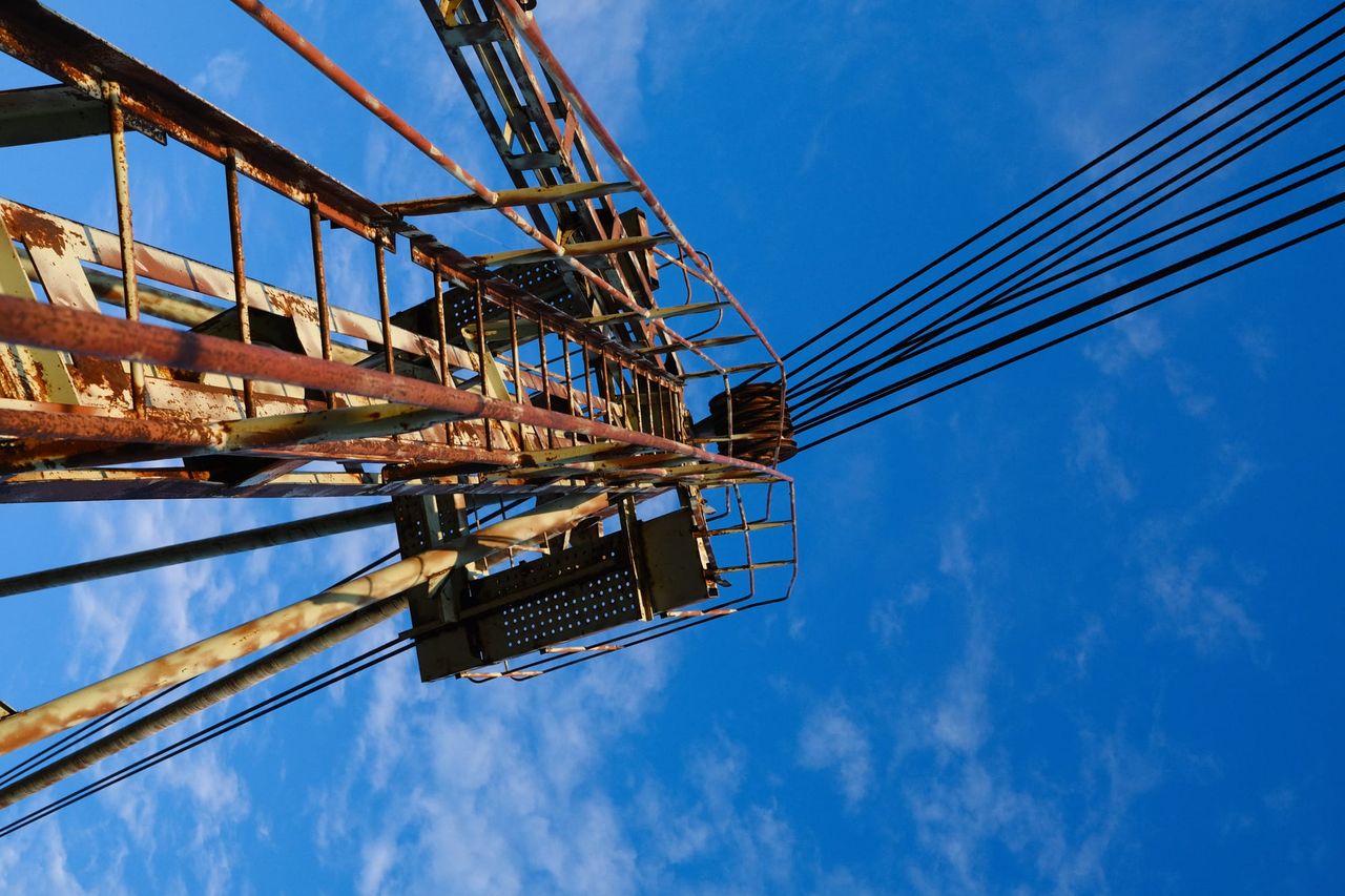 Cables densos y soportes metálicos cruzan diagonalmente un cielo azul intenso.