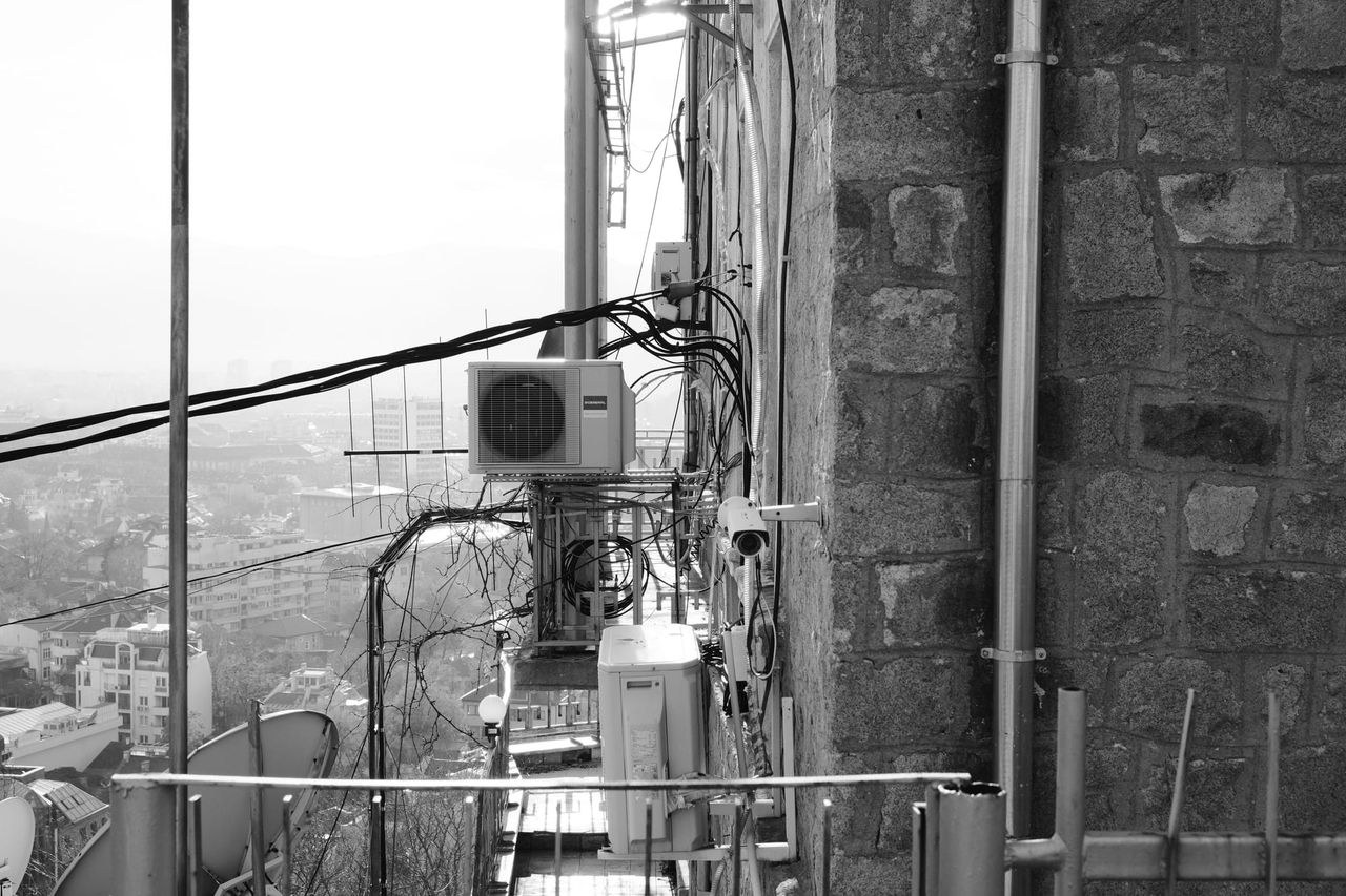 Pared de edificio con cableado exterior, tuberías y aire acondicionado en blanco y negro.