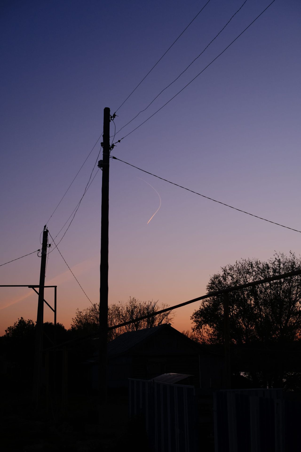 Postes y cables en silueta contra un crepúsculo violeta.