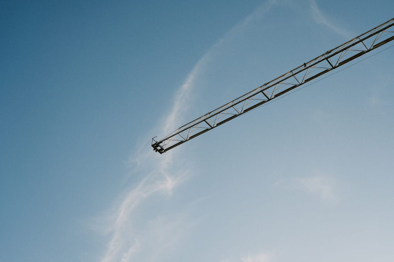 Lattice crane boom cuts diagonally across an open blue sky.