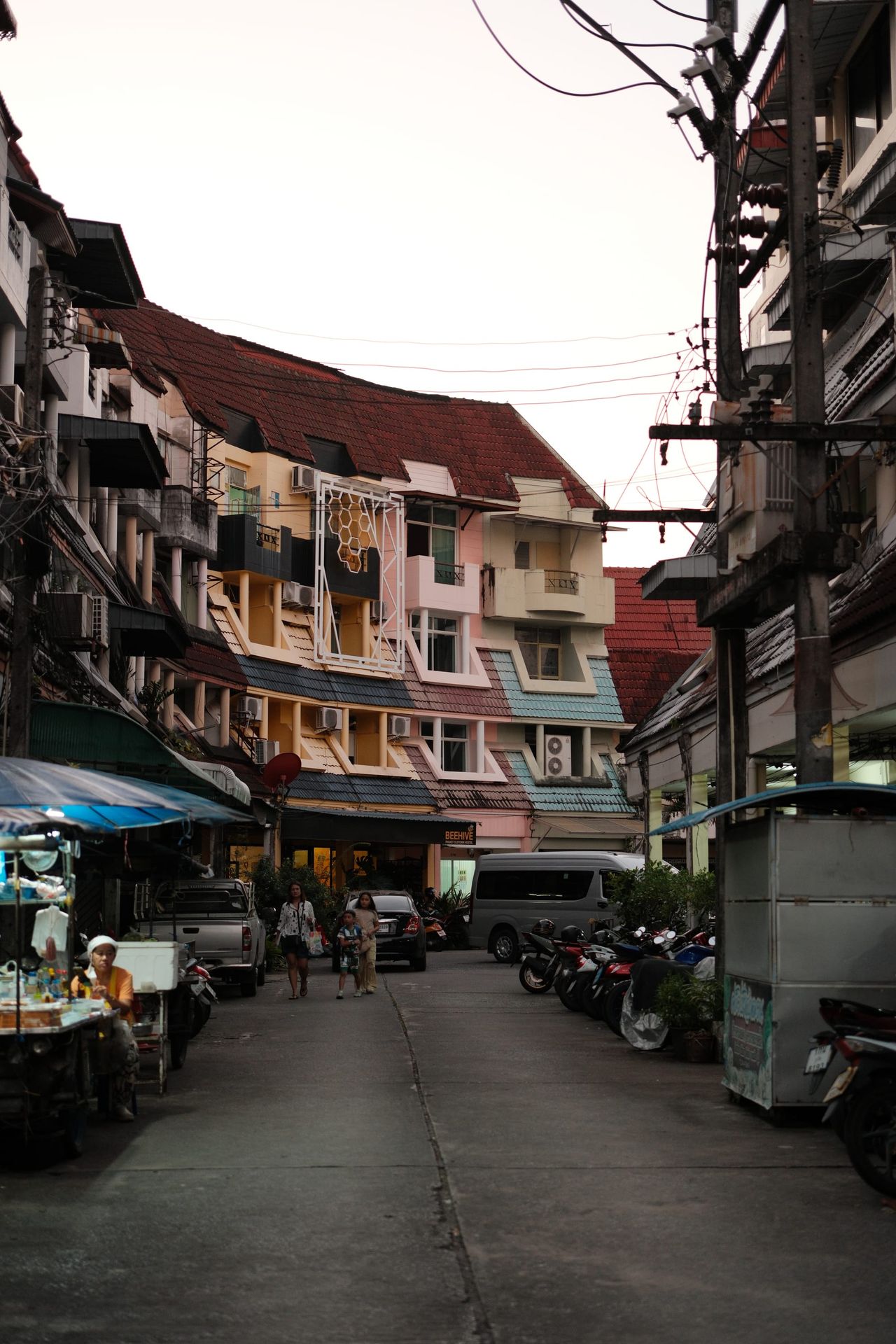 Calle estrecha con balcones, toldos, scooters y peatones.