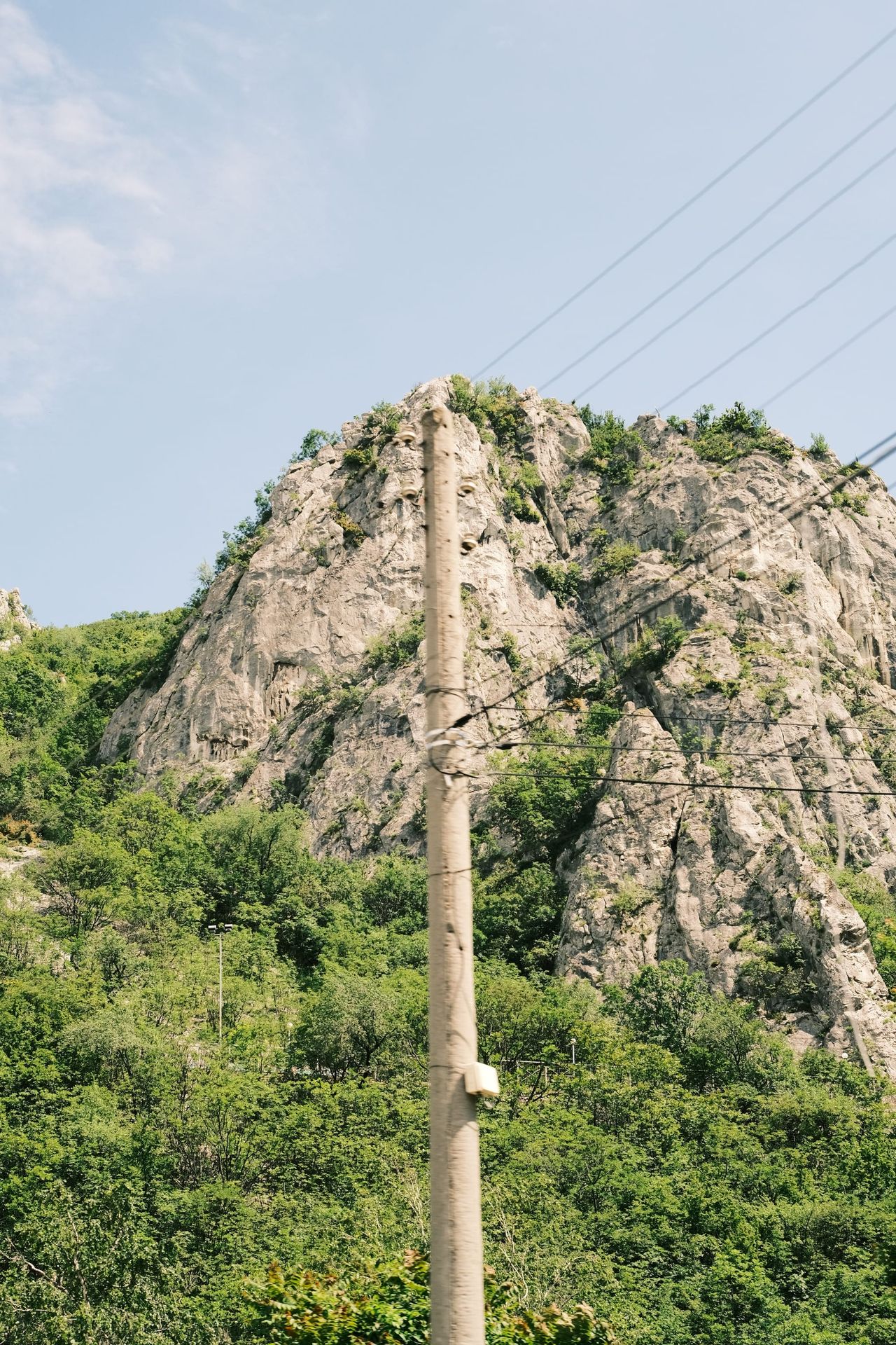Utility pole and wires interrupt a rugged green-dotted rock formation.