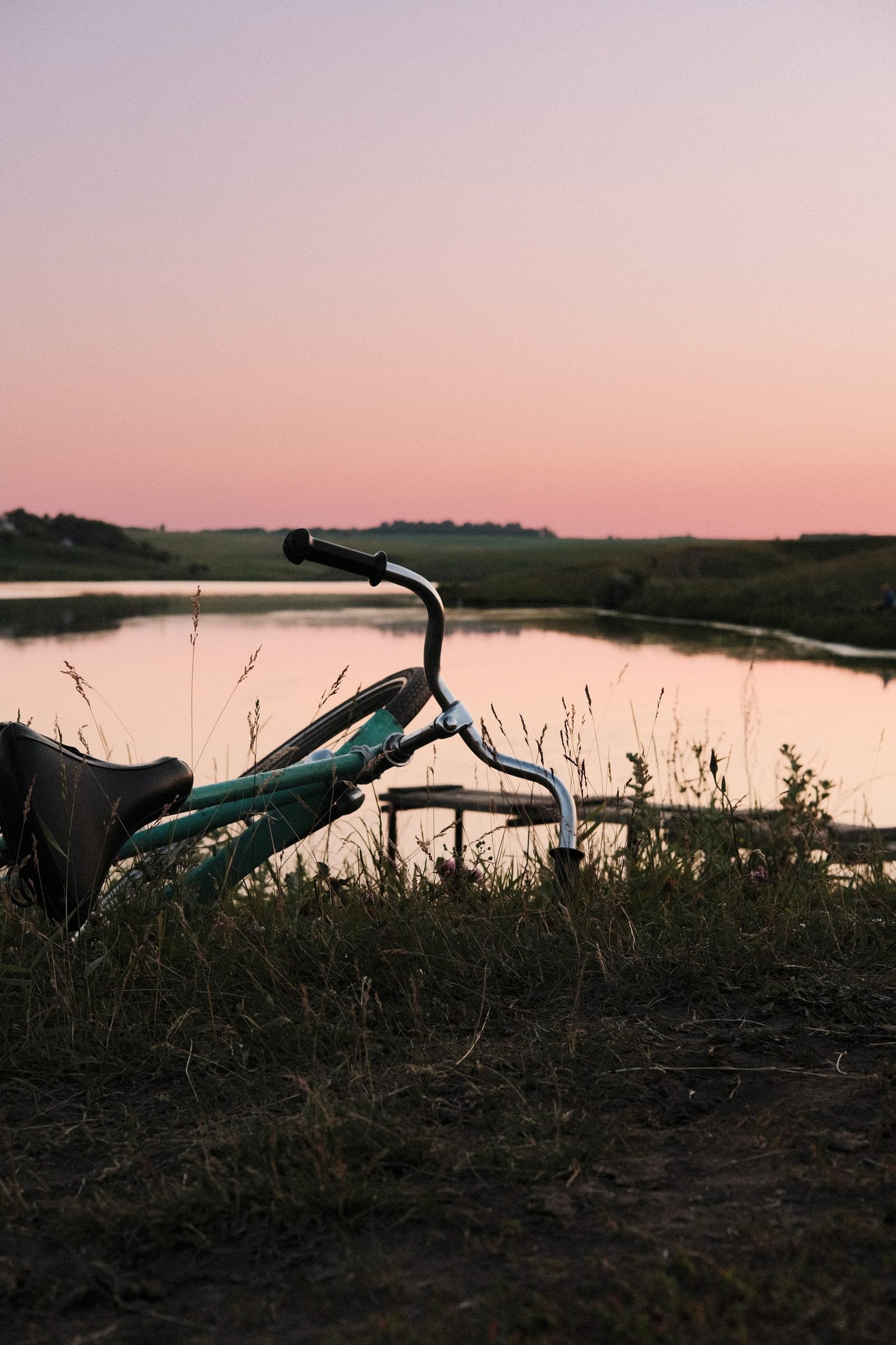 Bicycle beside a calm lake beneath a pastel pink and blue evening sky