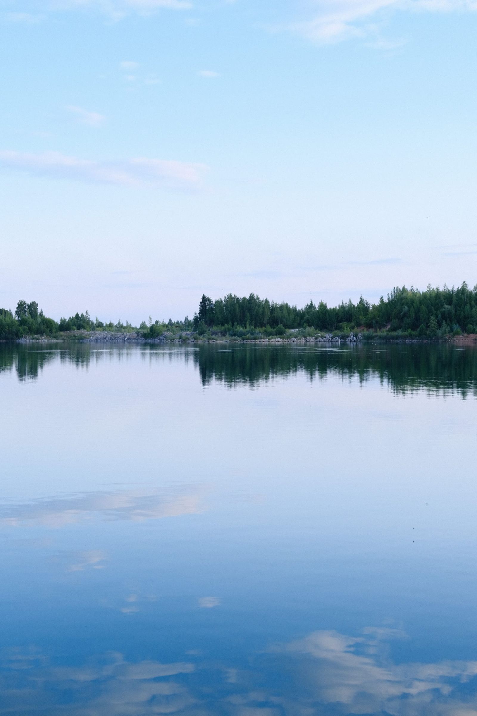 Calm lake reflecting a soft blue and pink sky beside a dark tree line
