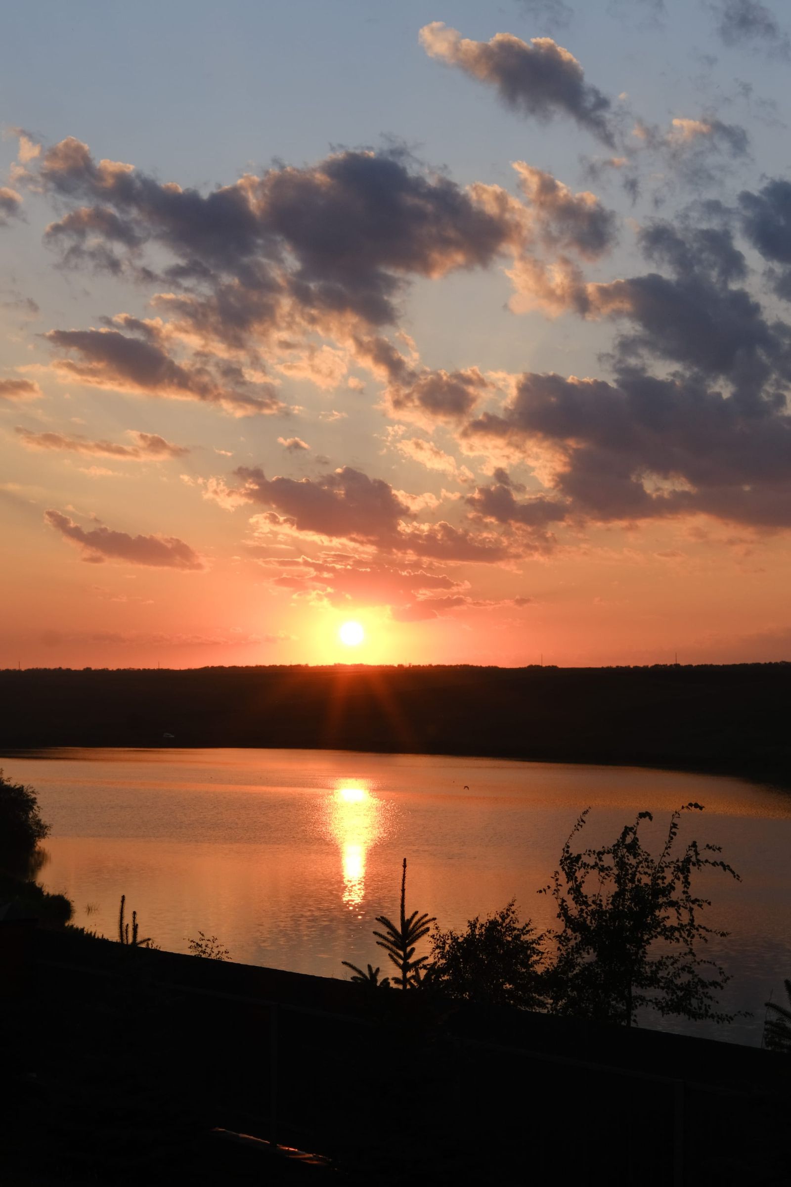 Orange sunset and dark clouds reflected across a still lake