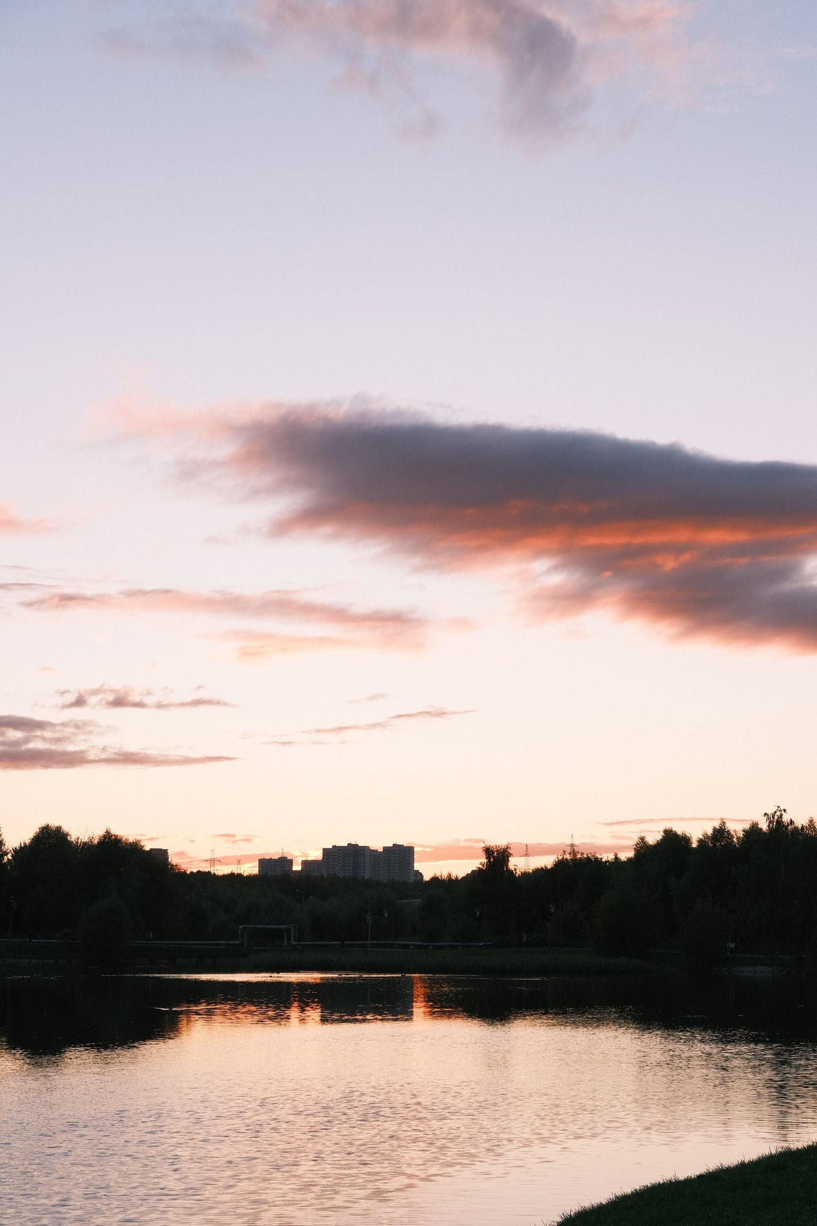 Long pink cloud above a calm river at dusk with trees in silhouette