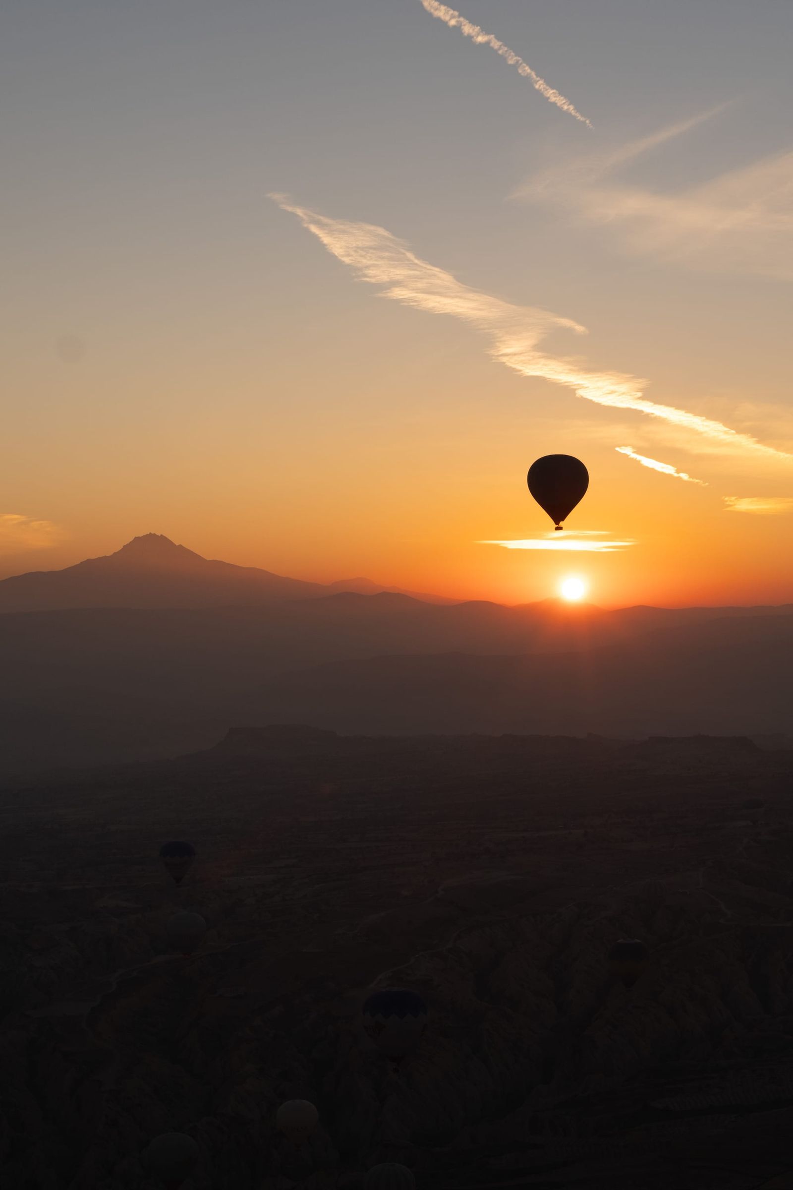 Single hot-air balloon crossing an orange sunset above dark mountain silhouettes