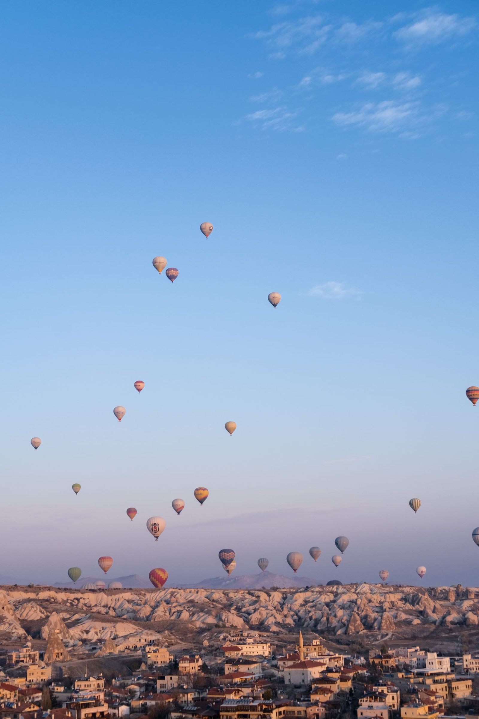 Dozens of hot-air balloons rising over a rocky town beneath a clear morning sky