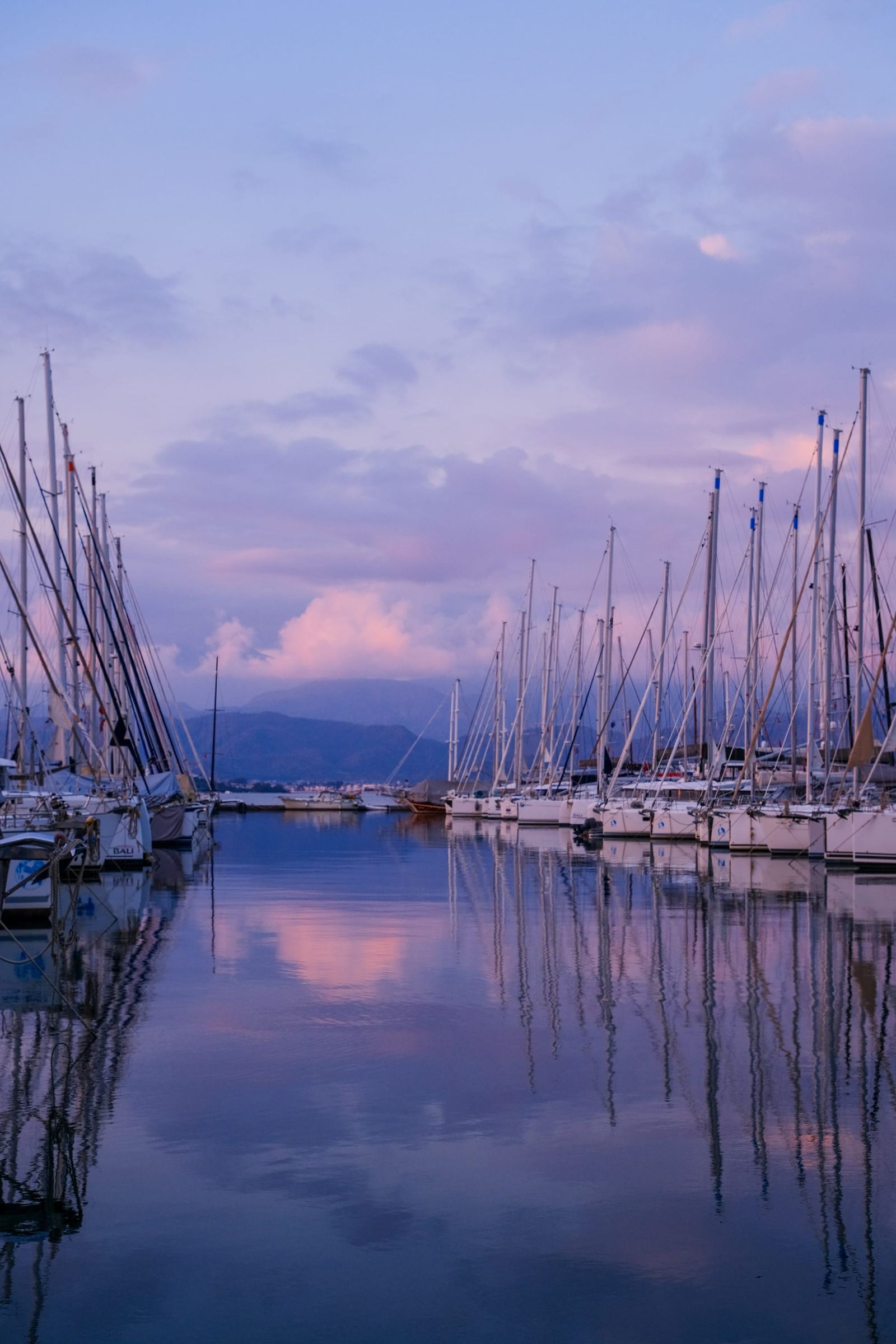 Sailboats and masts reflected in a marina beneath a lavender evening sky