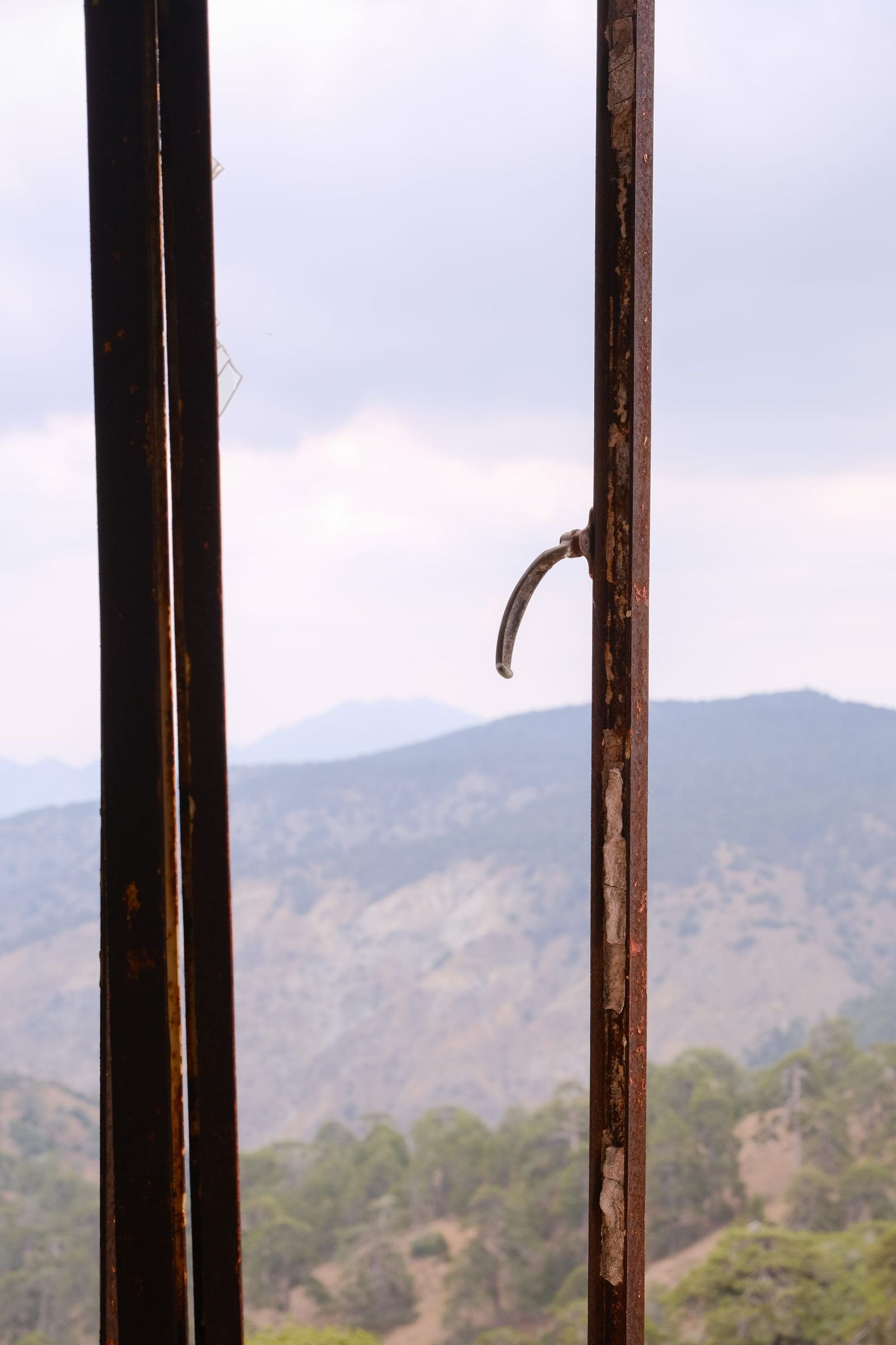 Open weathered window framing hazy mountain ridges beneath a pale sky