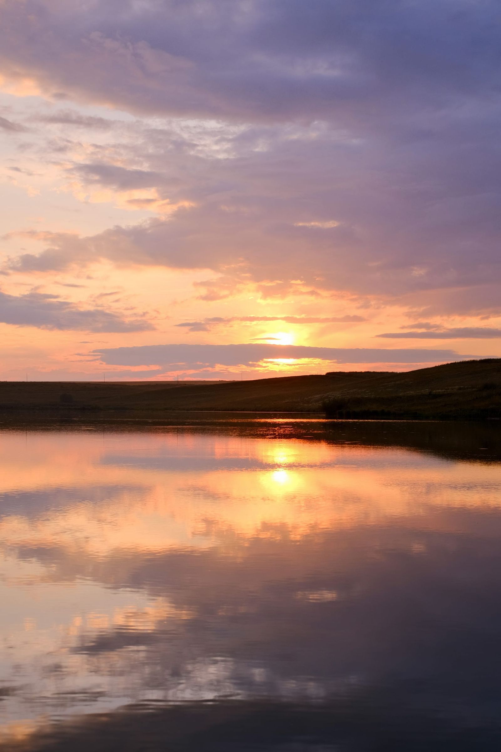 Golden sunset reflected in still water beneath layered purple clouds