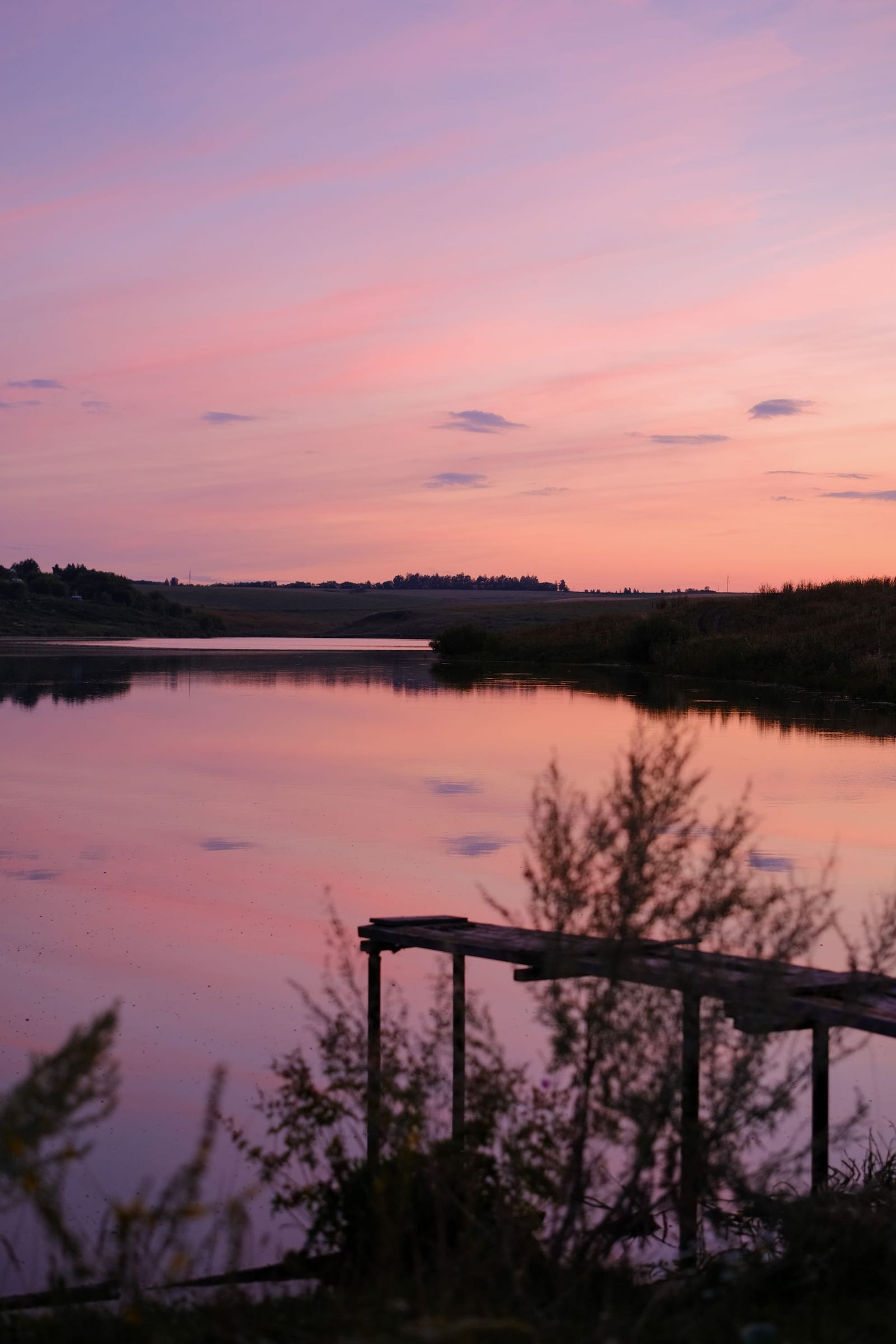 Pink dusk reflected in a calm river behind a silhouetted wooden frame