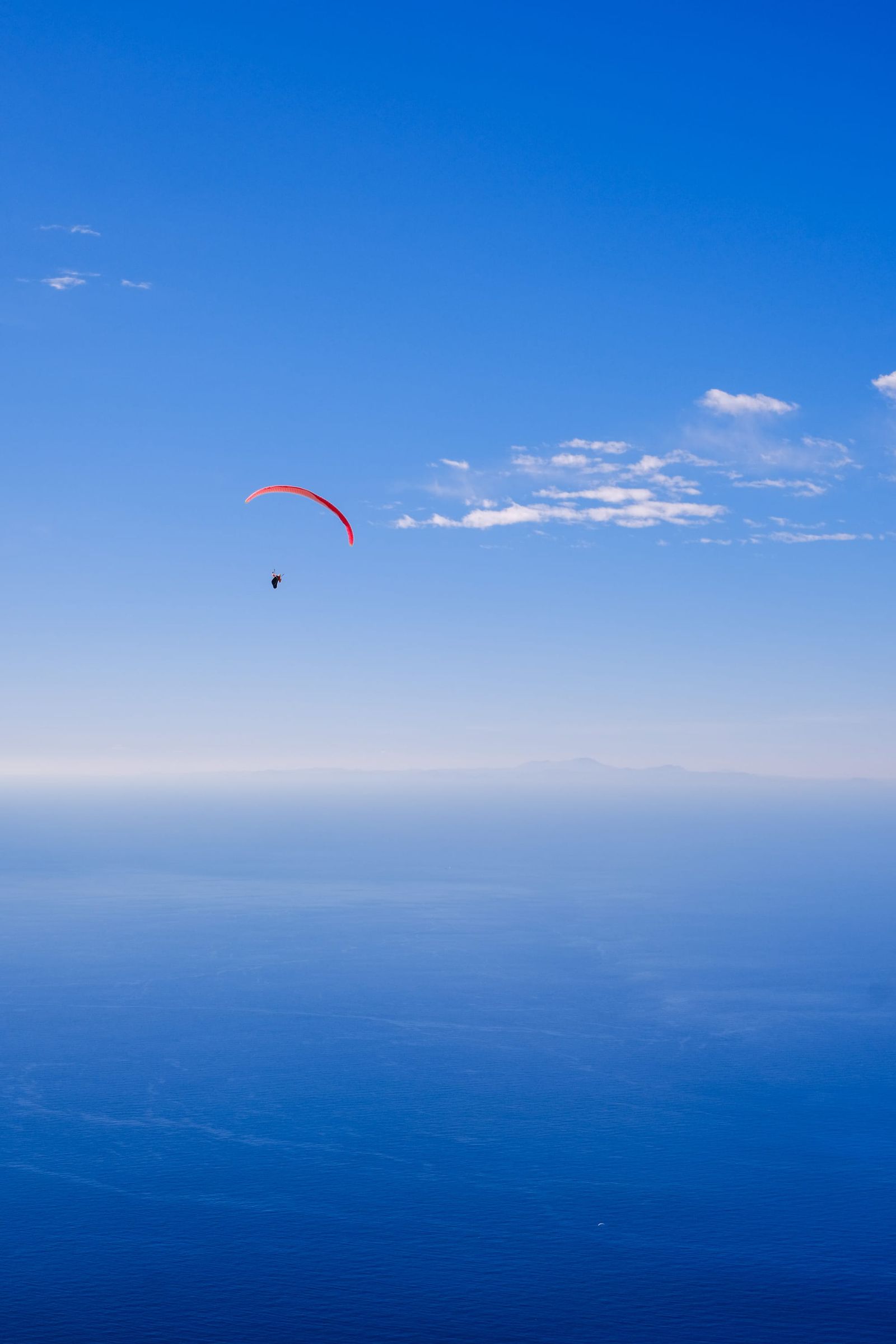 Paraglider suspended above a deep blue sea beneath a clear sky
