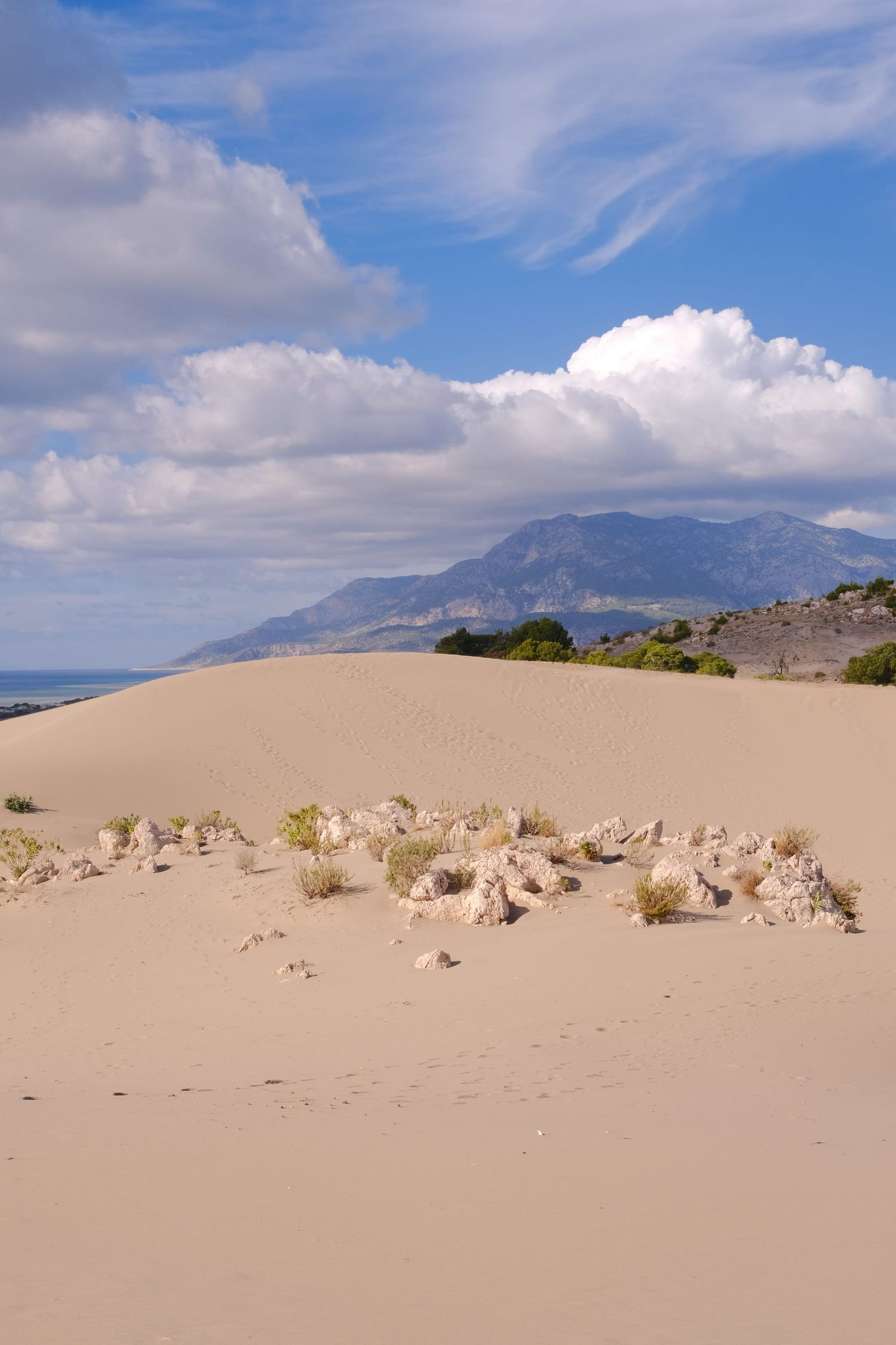 Pale sand dunes leading toward rugged mountains beneath billowing white clouds