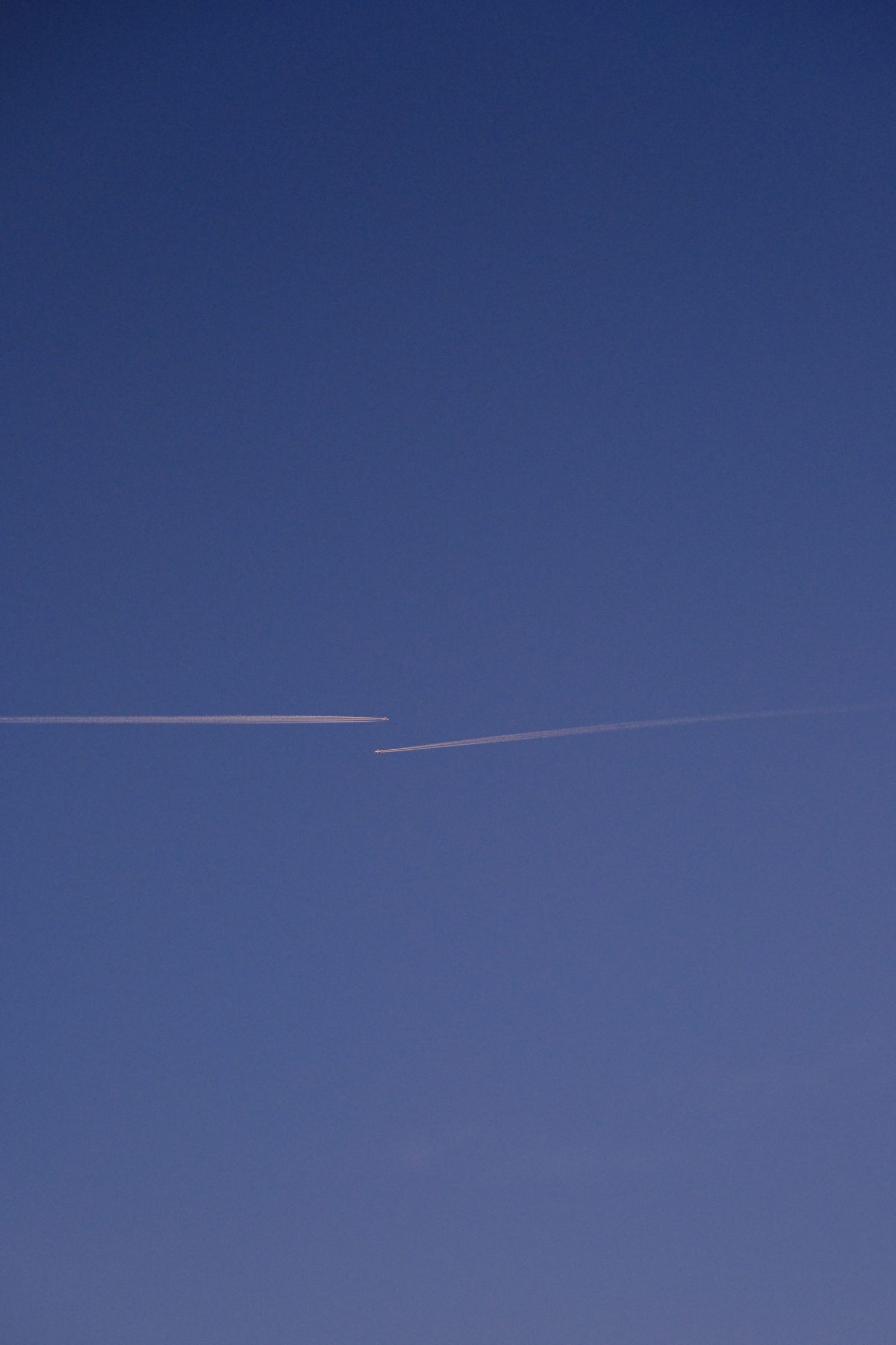 Parallel aircraft trails cutting across a dark blue twilight sky