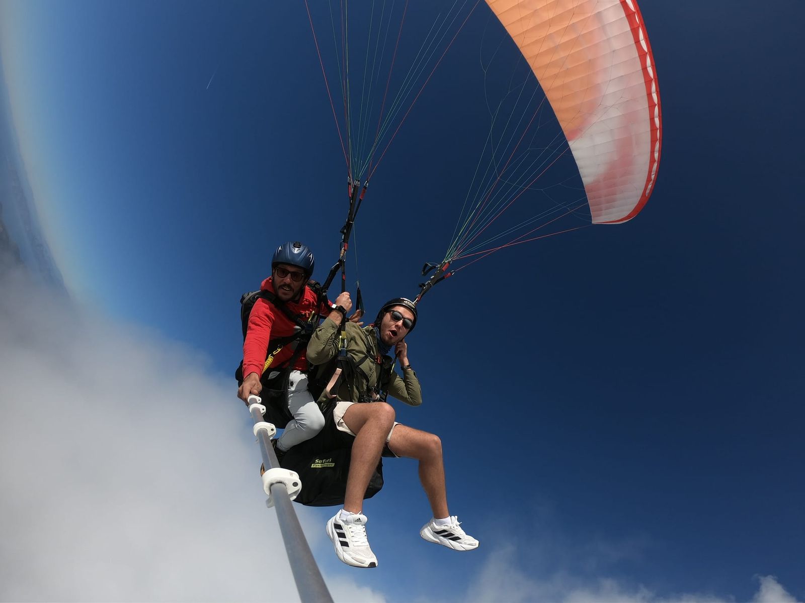Tandem pair beneath the orange paraglider canopy in clear blue sky