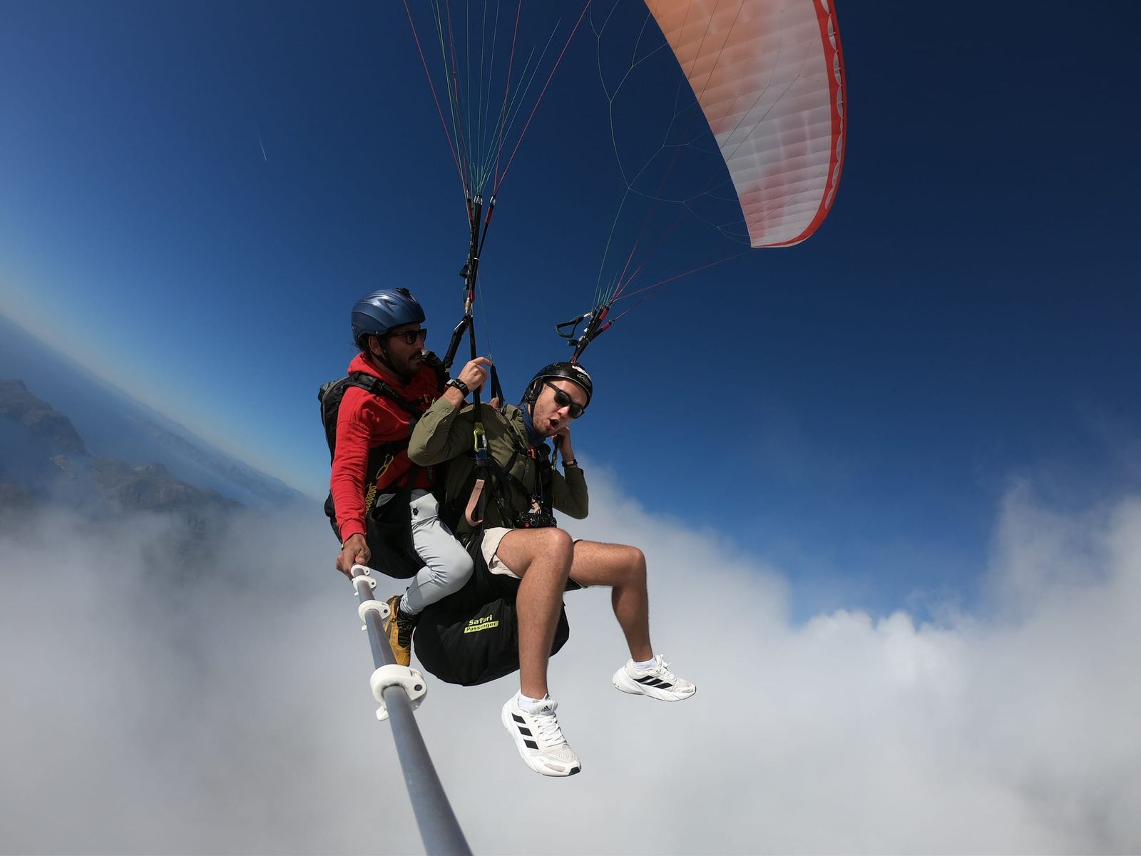 Tandem paragliders gliding along the edge of a bright cloud
