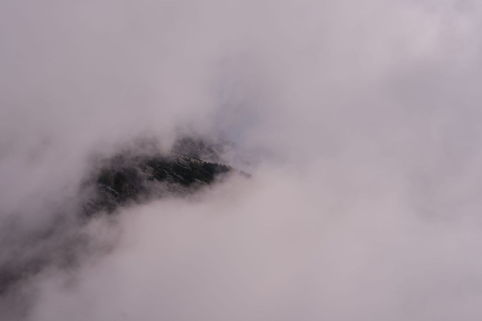 Dense white cloud opening briefly over the rocky mountainside