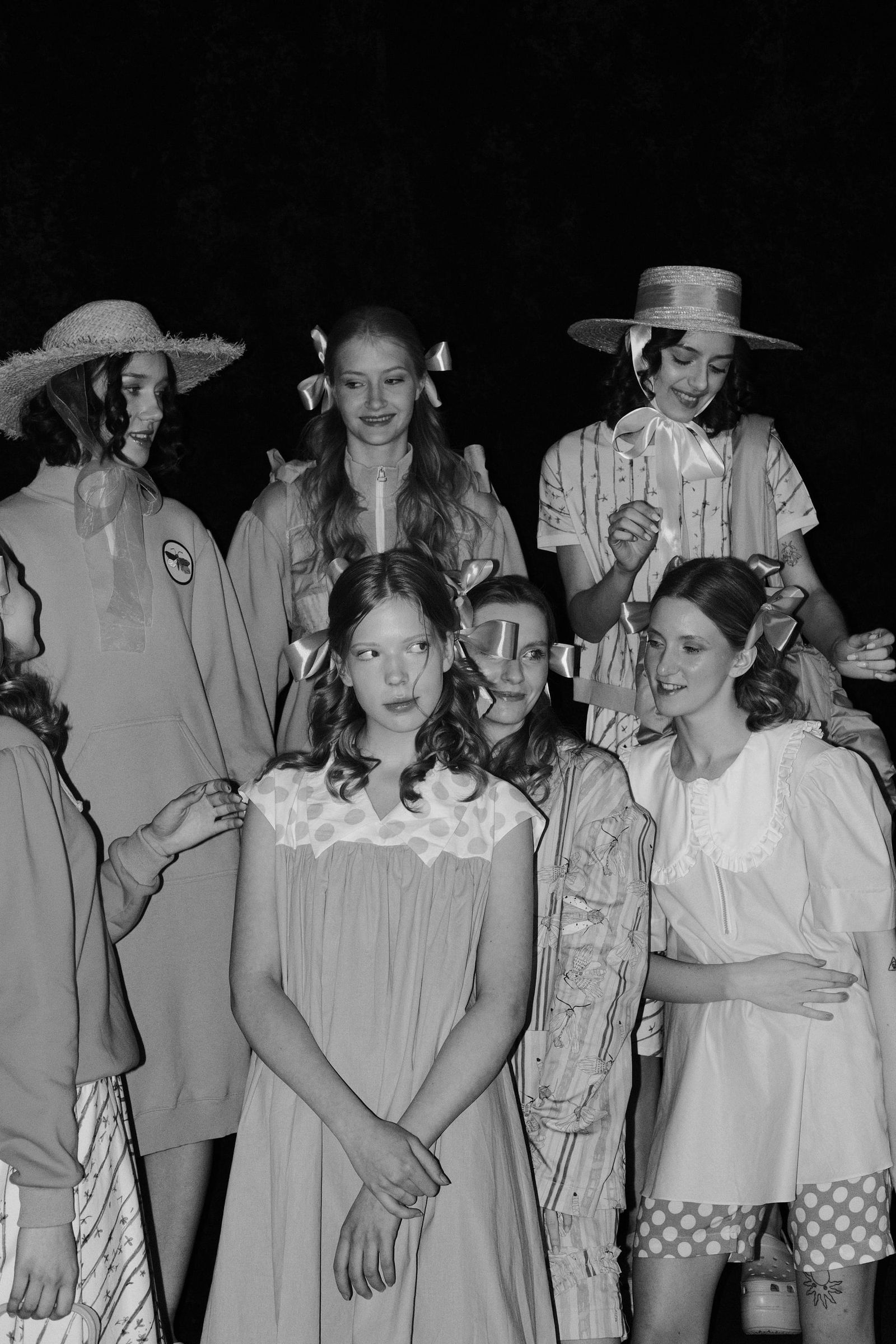 Black-and-white photograph of a group of models in dresses, blouses and brimmed hats at the end of the runway.