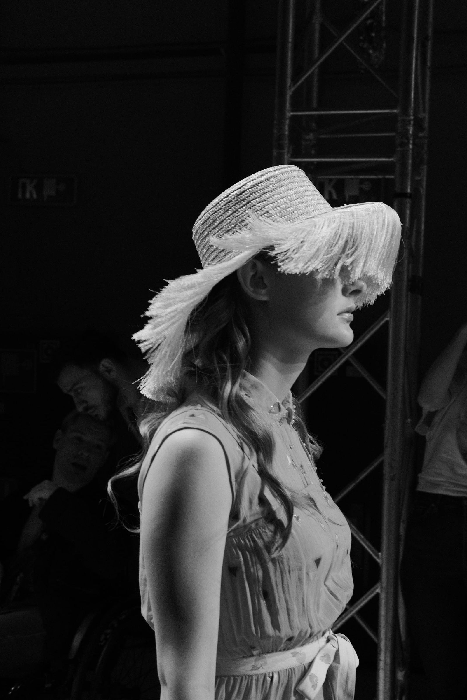 Black-and-white side view of a model in a broad floppy hat and sleeveless outfit.