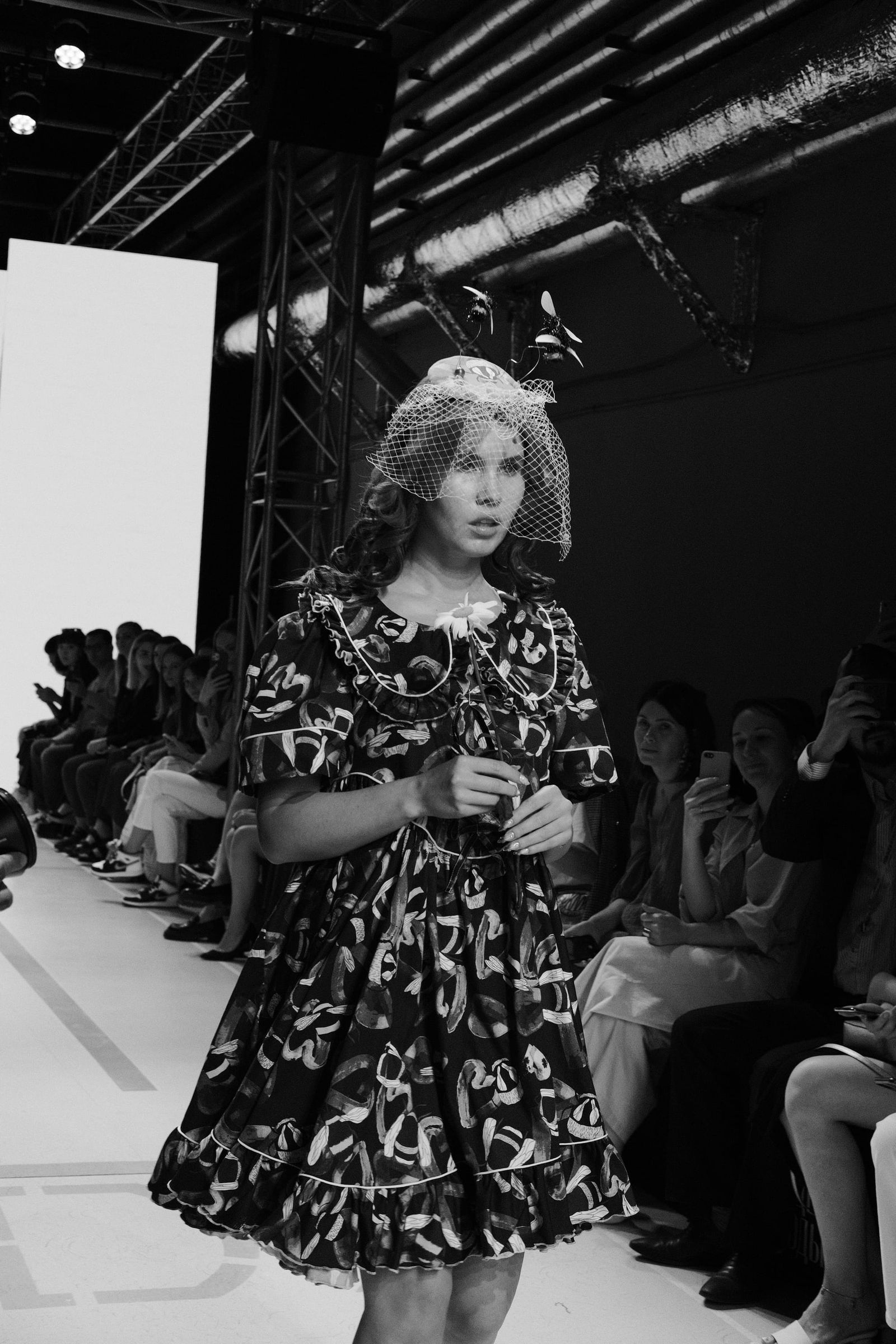 Black-and-white photograph of a model in a dark floral dress and a large hair bow.