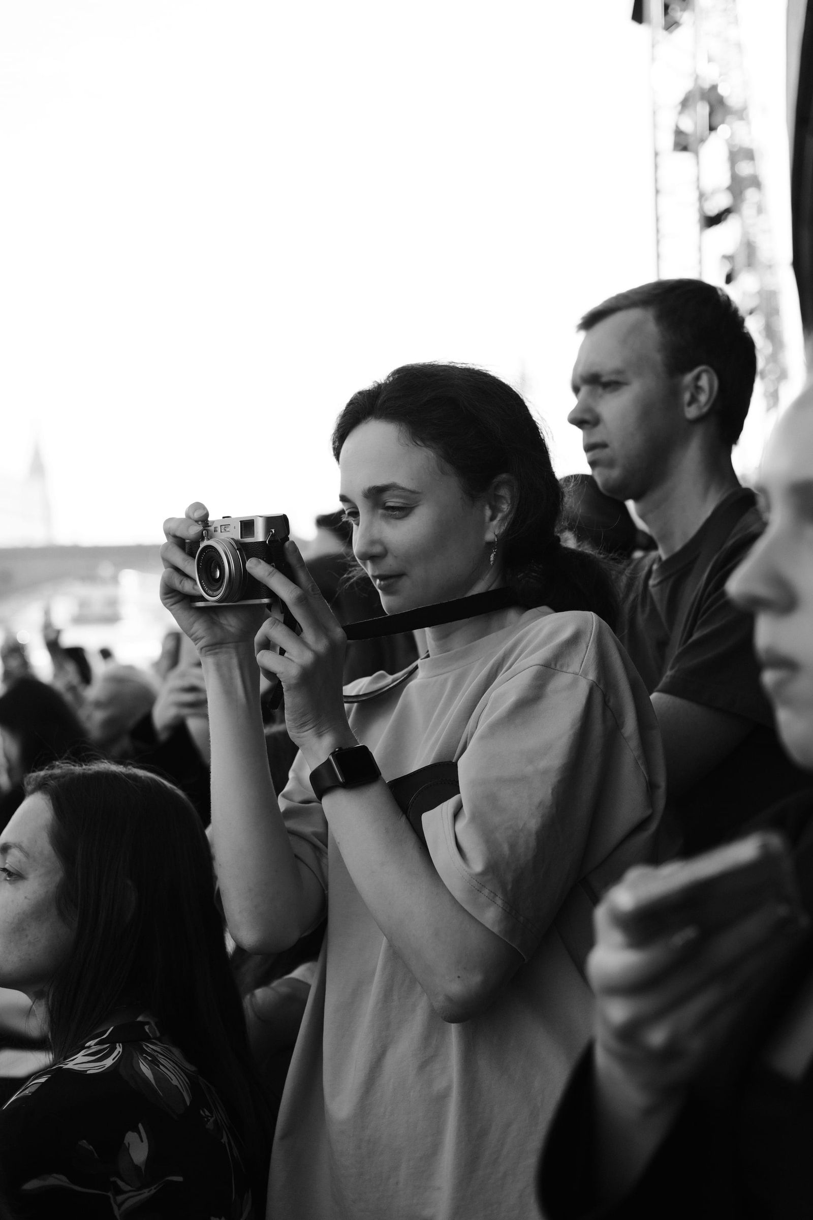 A seated spectator holds up a phone to photograph the show in a black-and-white image.