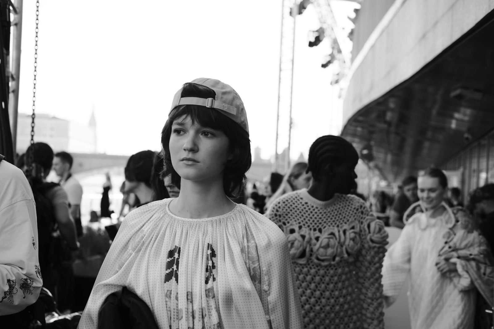 A model in a backward cap and a light printed top walks ahead of other models in black and white.