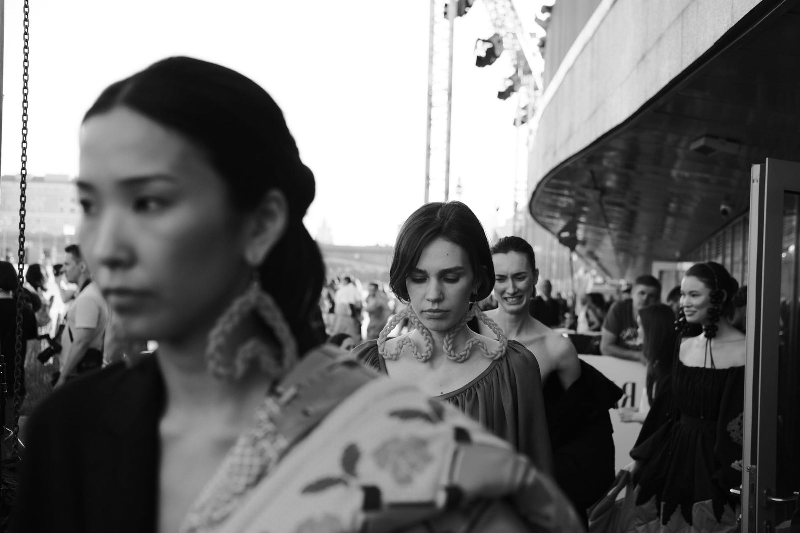 Black-and-white view of models walking through a crowd, with a foreground face softly out of focus.