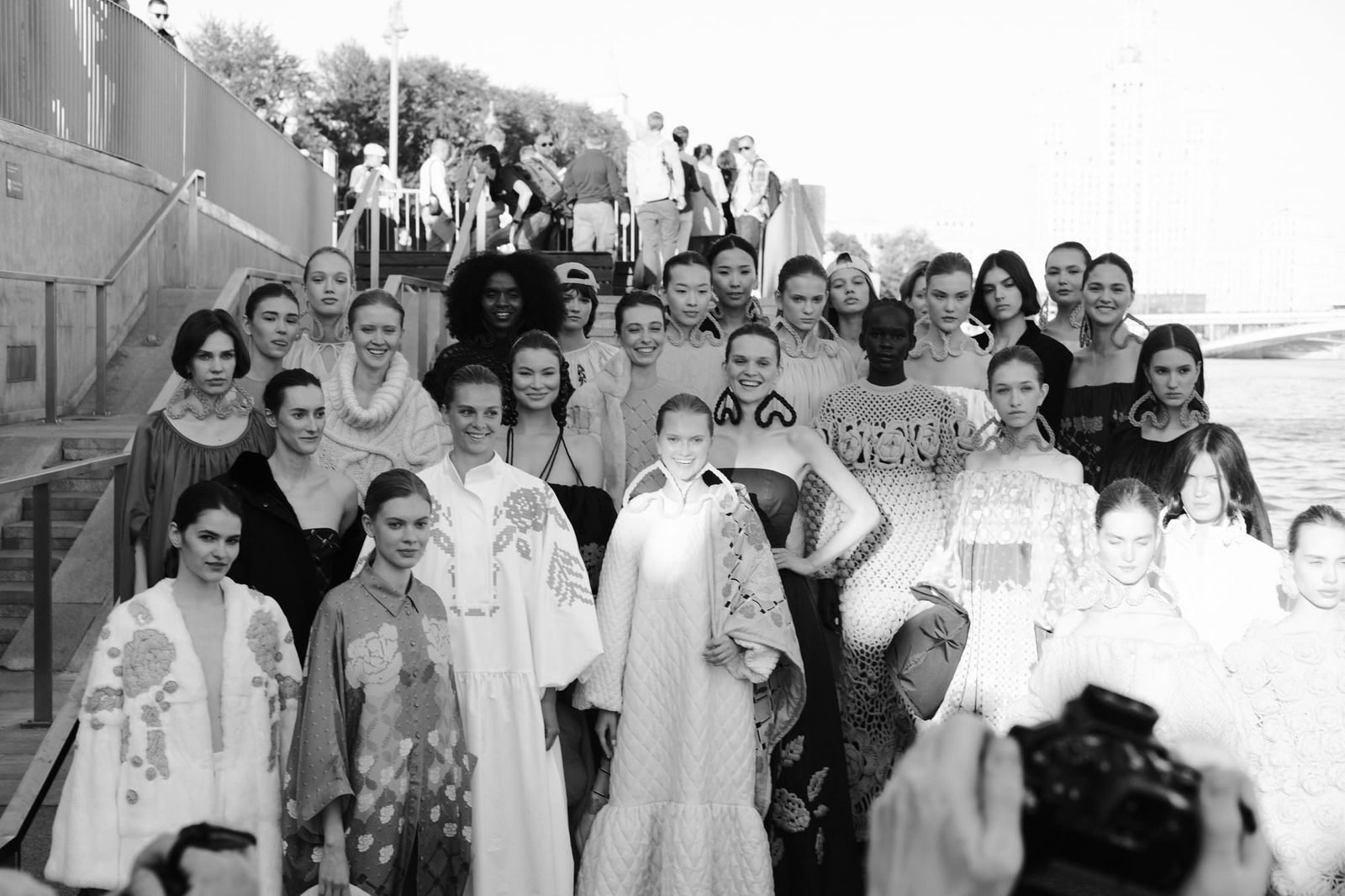 A large group of models poses together on outdoor steps in a black-and-white photograph.