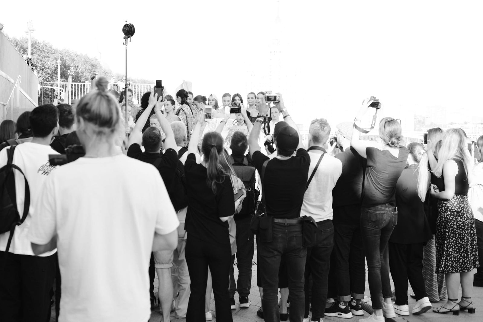 An outdoor crowd gathers for photographs beside the venue in a wide black-and-white view.