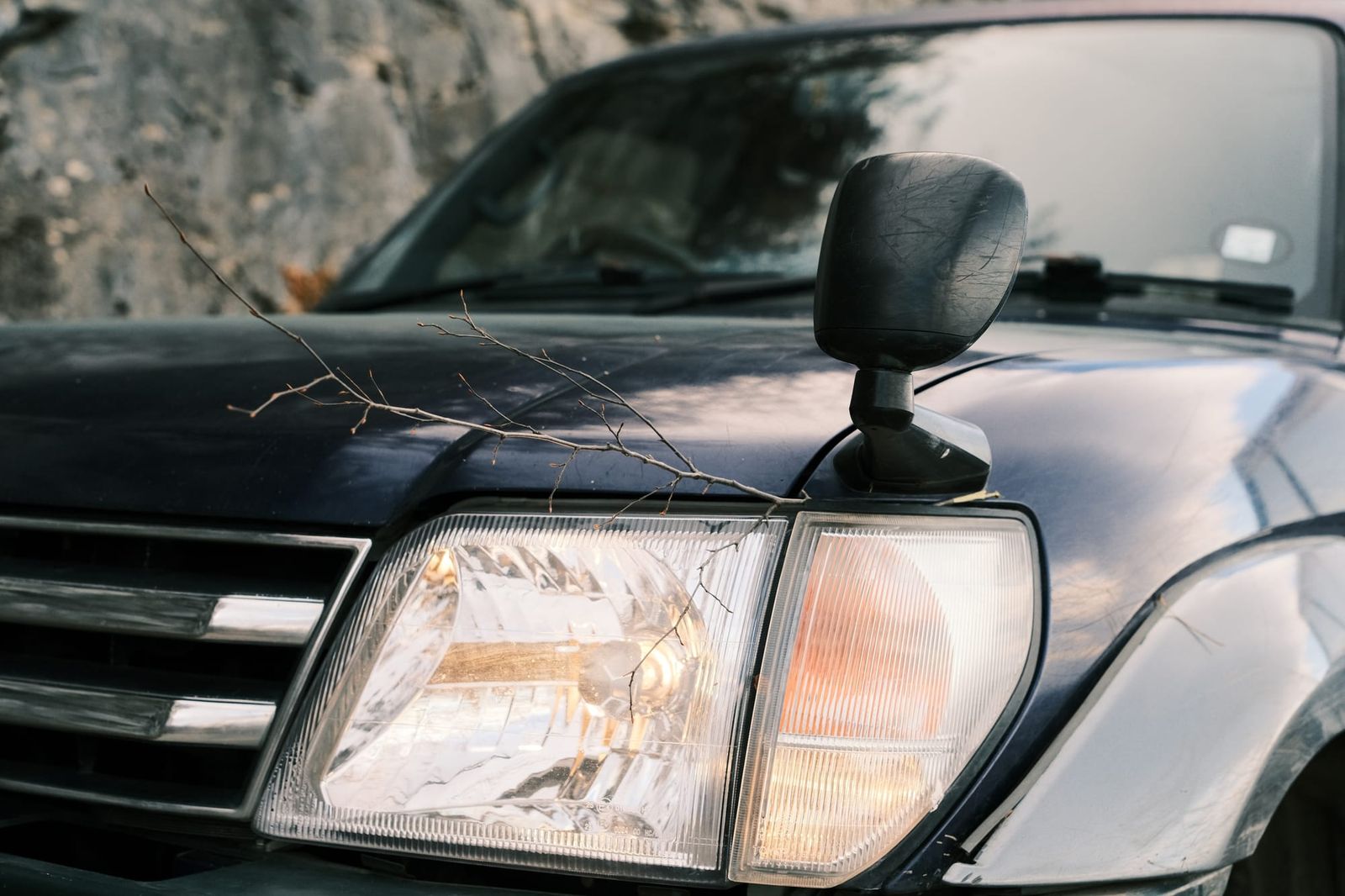 Close view of a Toyota’s headlight, grille and wing mirror beside a rocky slope.