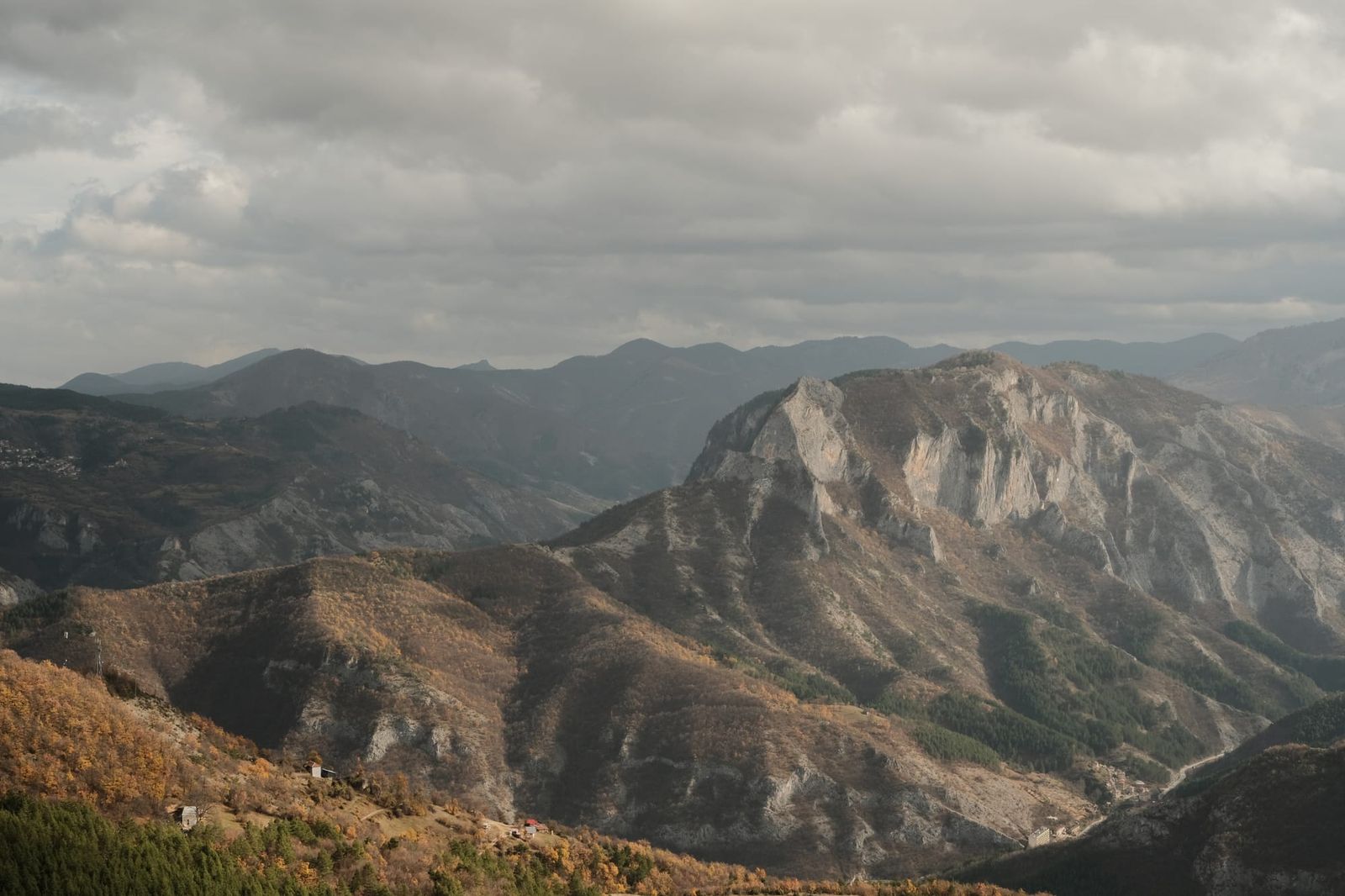 A pale, steep-sided mountain rises beneath dark clouds above surrounding forested ridges.