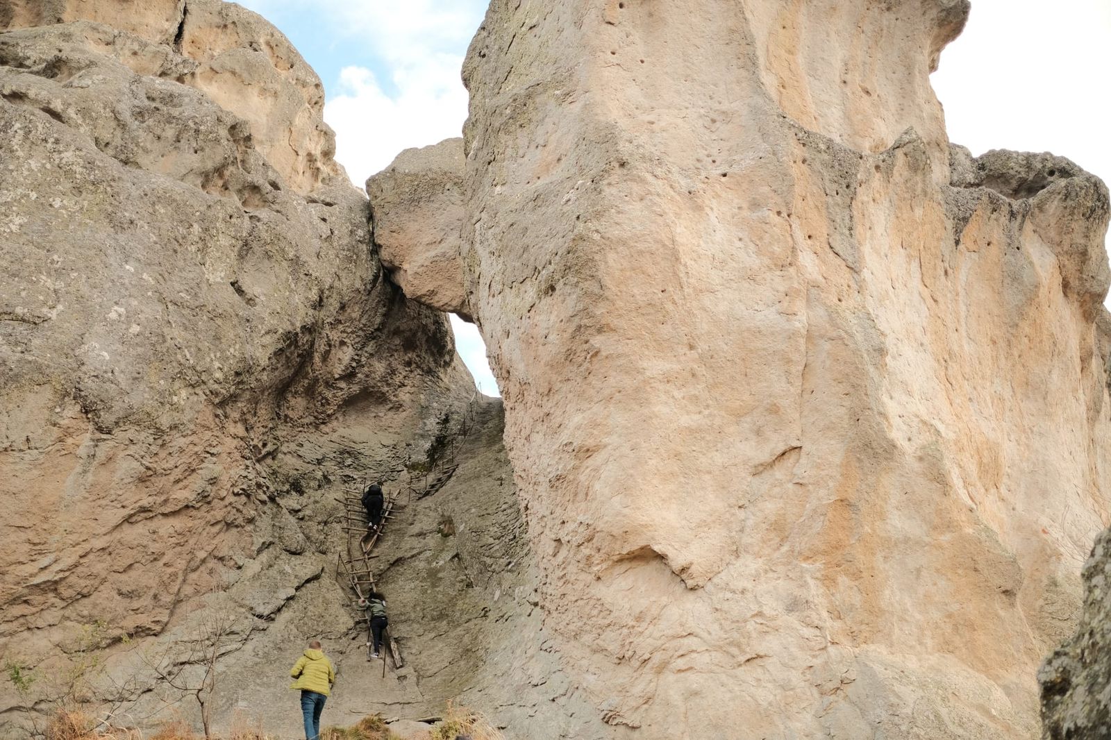 A small figure stands beneath towering pale rock walls separated by a narrow opening.