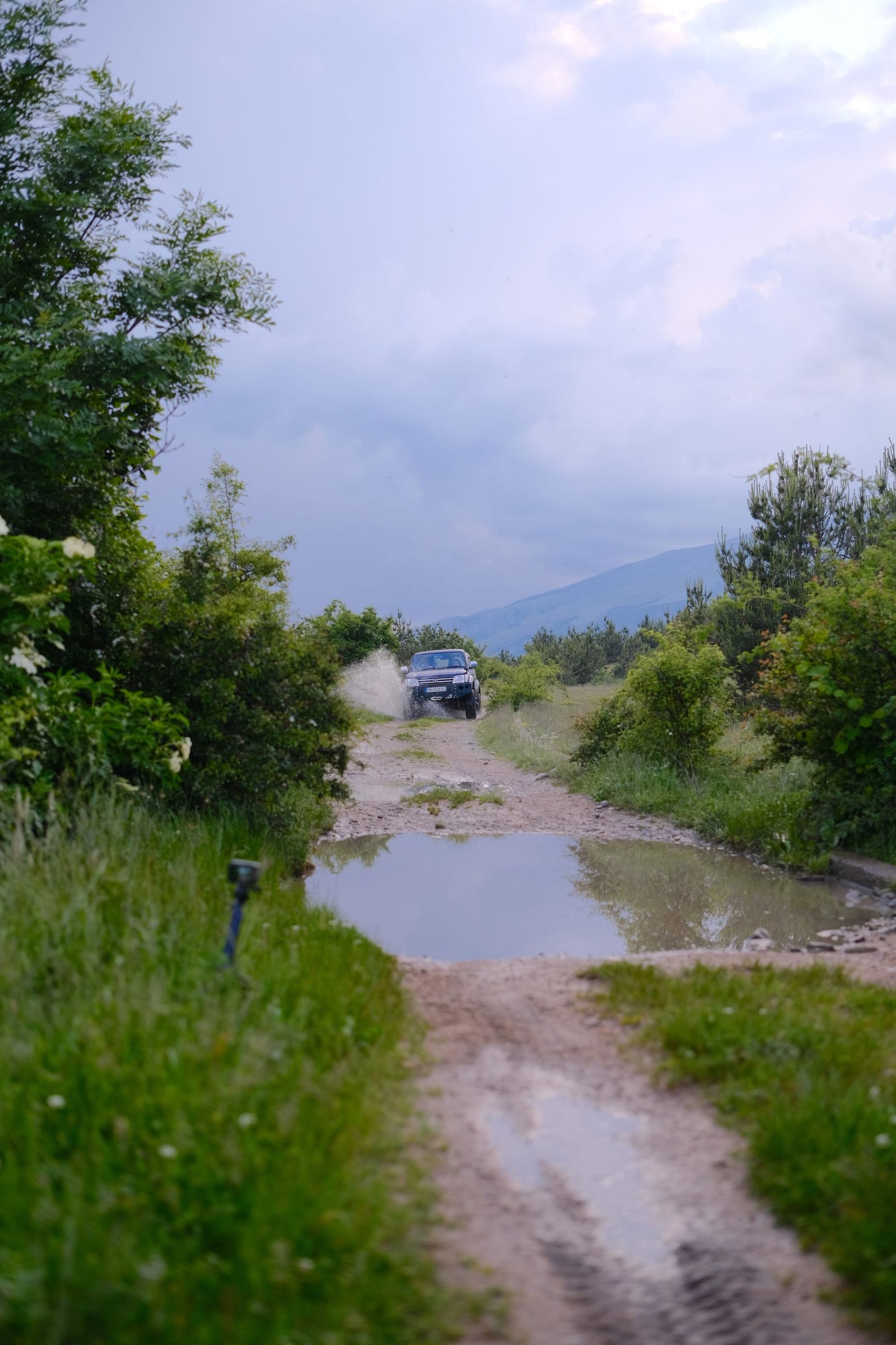 Four-wheel-drive vehicle approaching a broad puddle on a dirt road