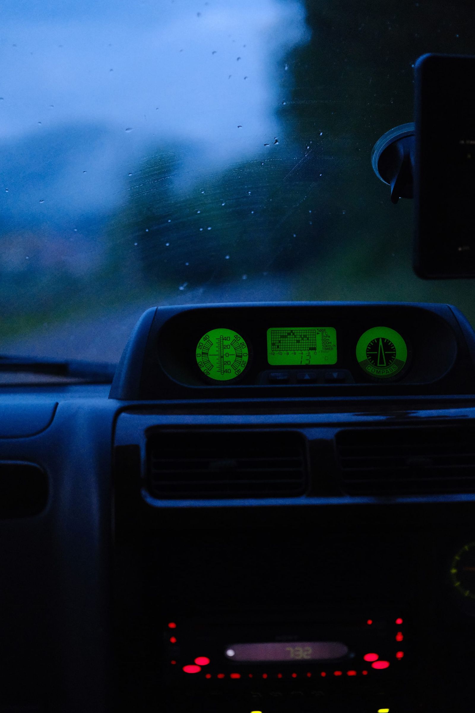 Car dashboard glowing green during a rainy twilight drive