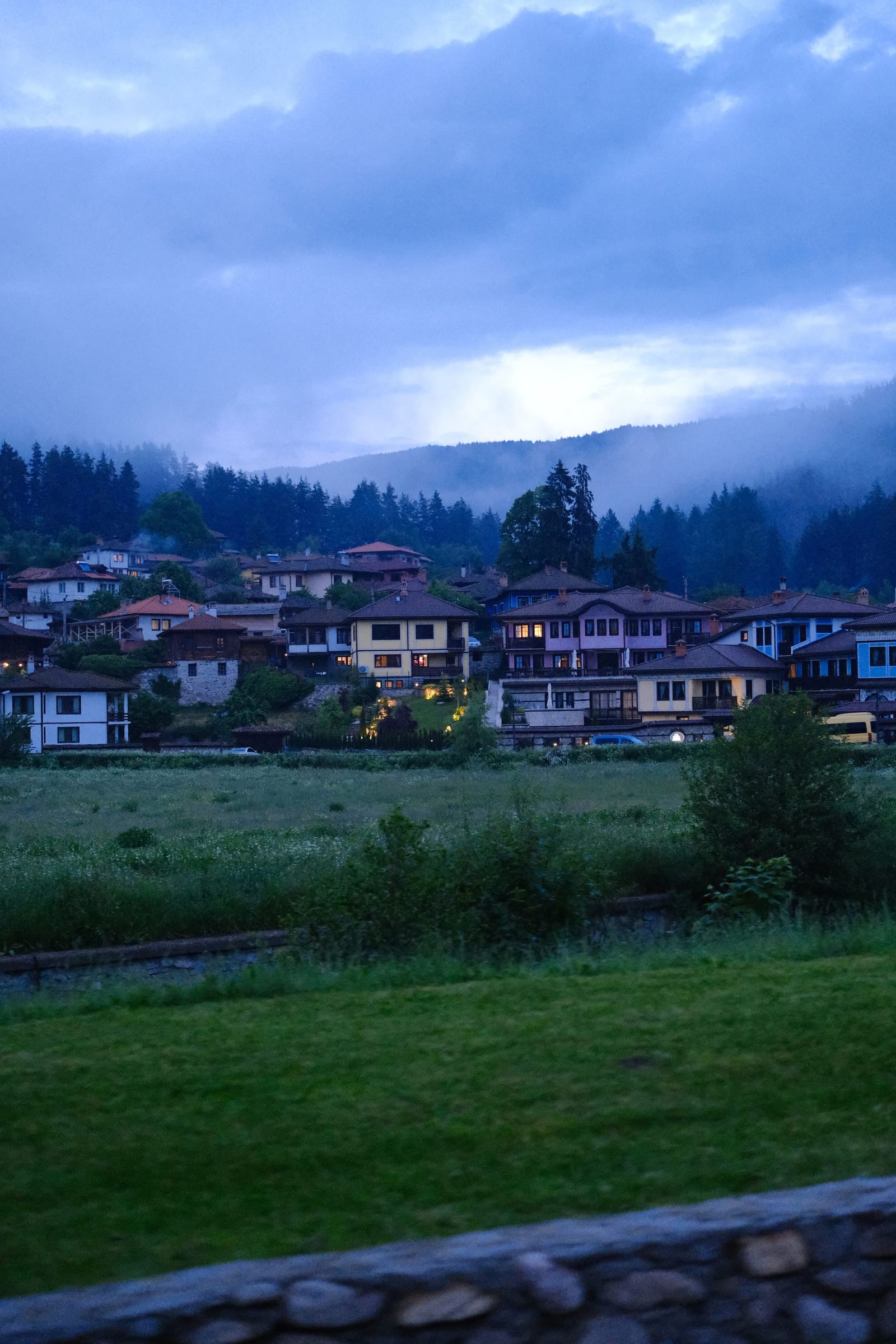 Bulgarian mountain village beneath a blue, cloud-heavy evening sky