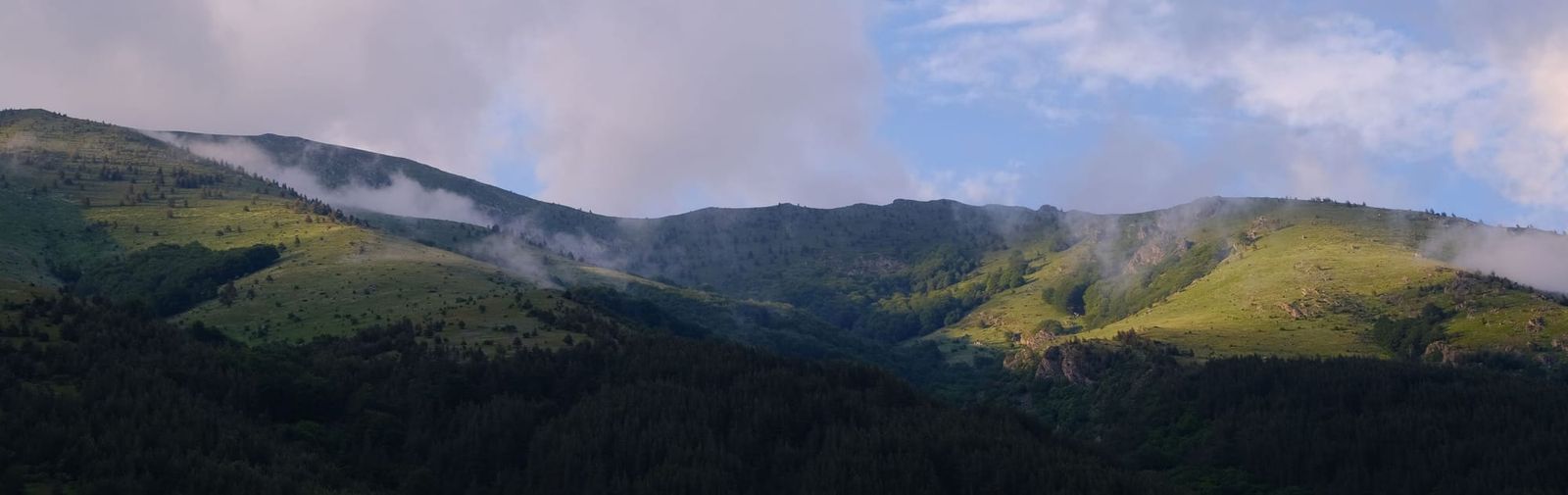 Late sunlight touching green mountain ridges beneath dark clouds