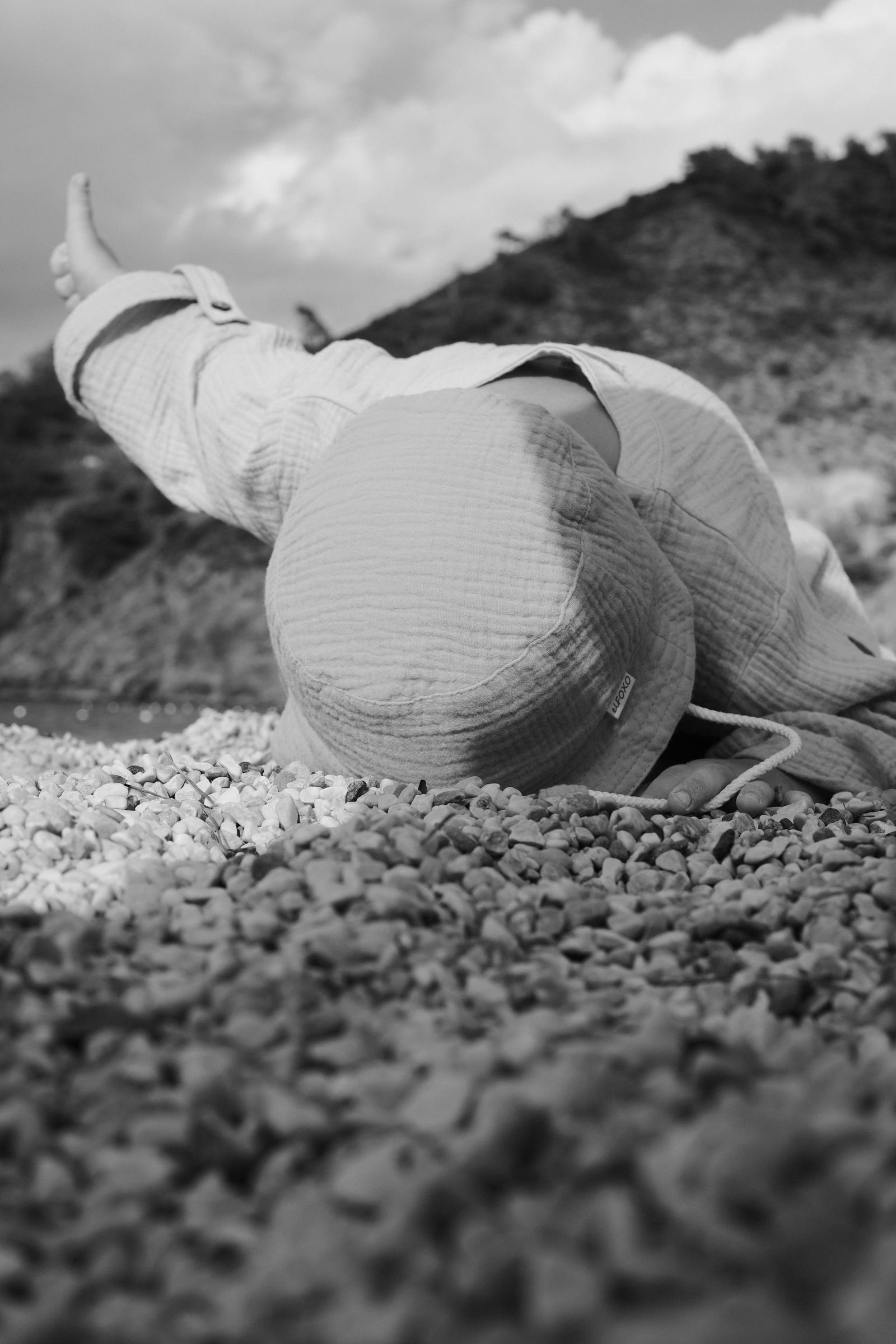 Child lying on a pebbled beach in a black-and-white photograph